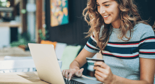 A smiling woman holds a credit card in one hand and types on a laptop with the other hand.