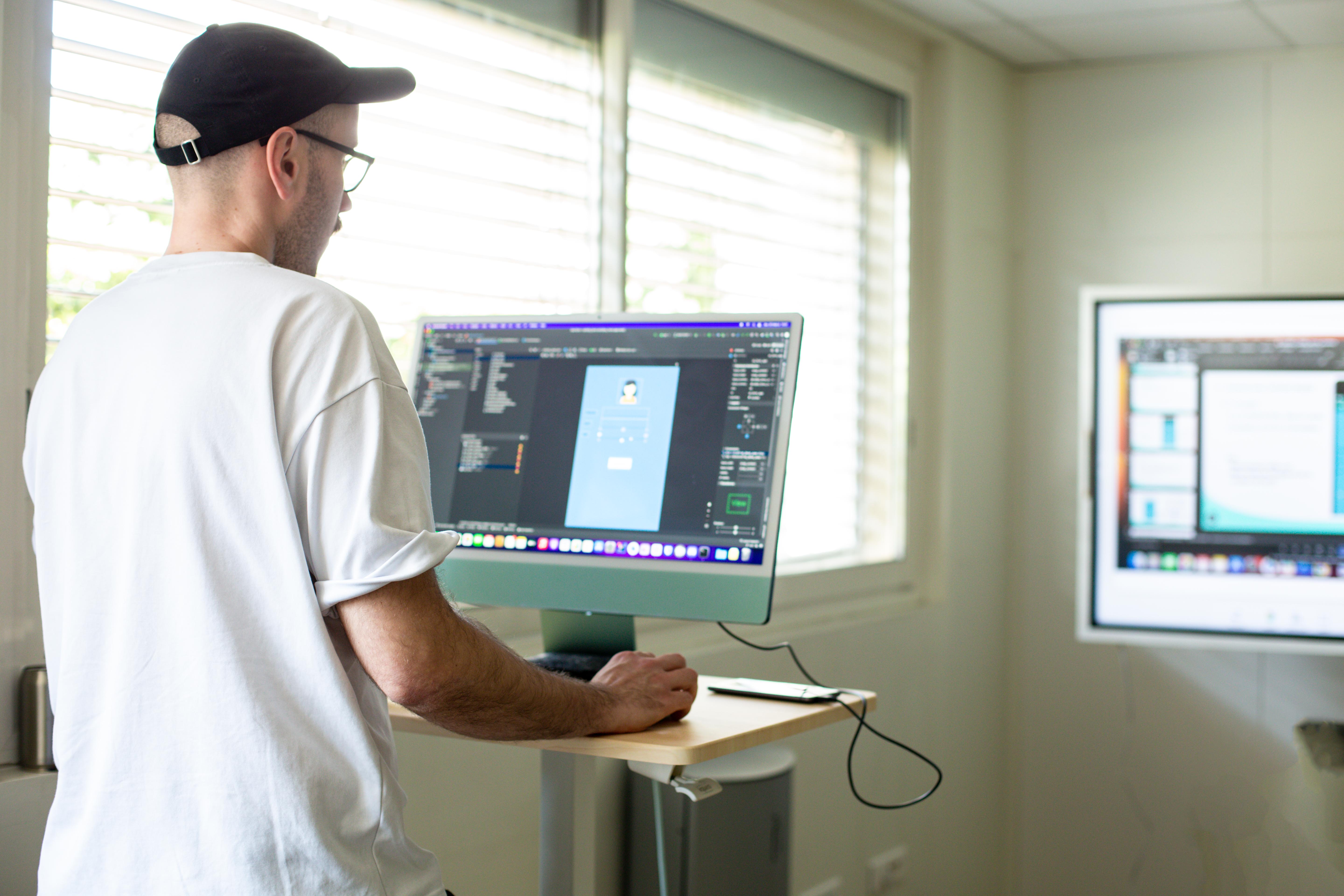 Homme de dos avec une casquette travaillant sur un ordinateur qui utilise un logiciel de développement.