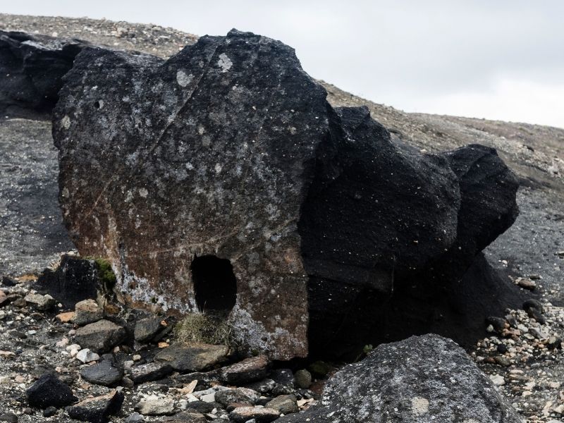 Large black obsidian rock in Hrafntinnusker mountain valley, Iceland, formed from rapidly cooled rhyolite lava, with a glassy texture and rugged volcanic landscape in the background.