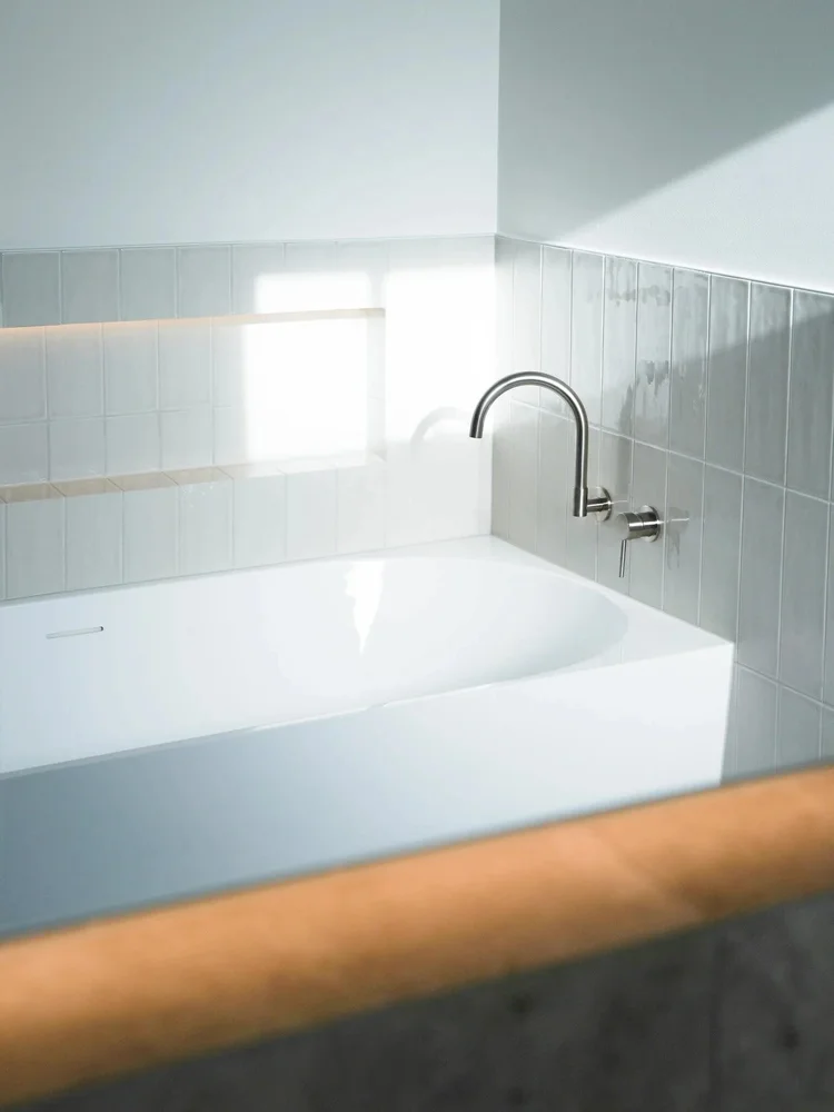 Modern white bathtub with sleek chrome faucet in a minimalist bathroom.