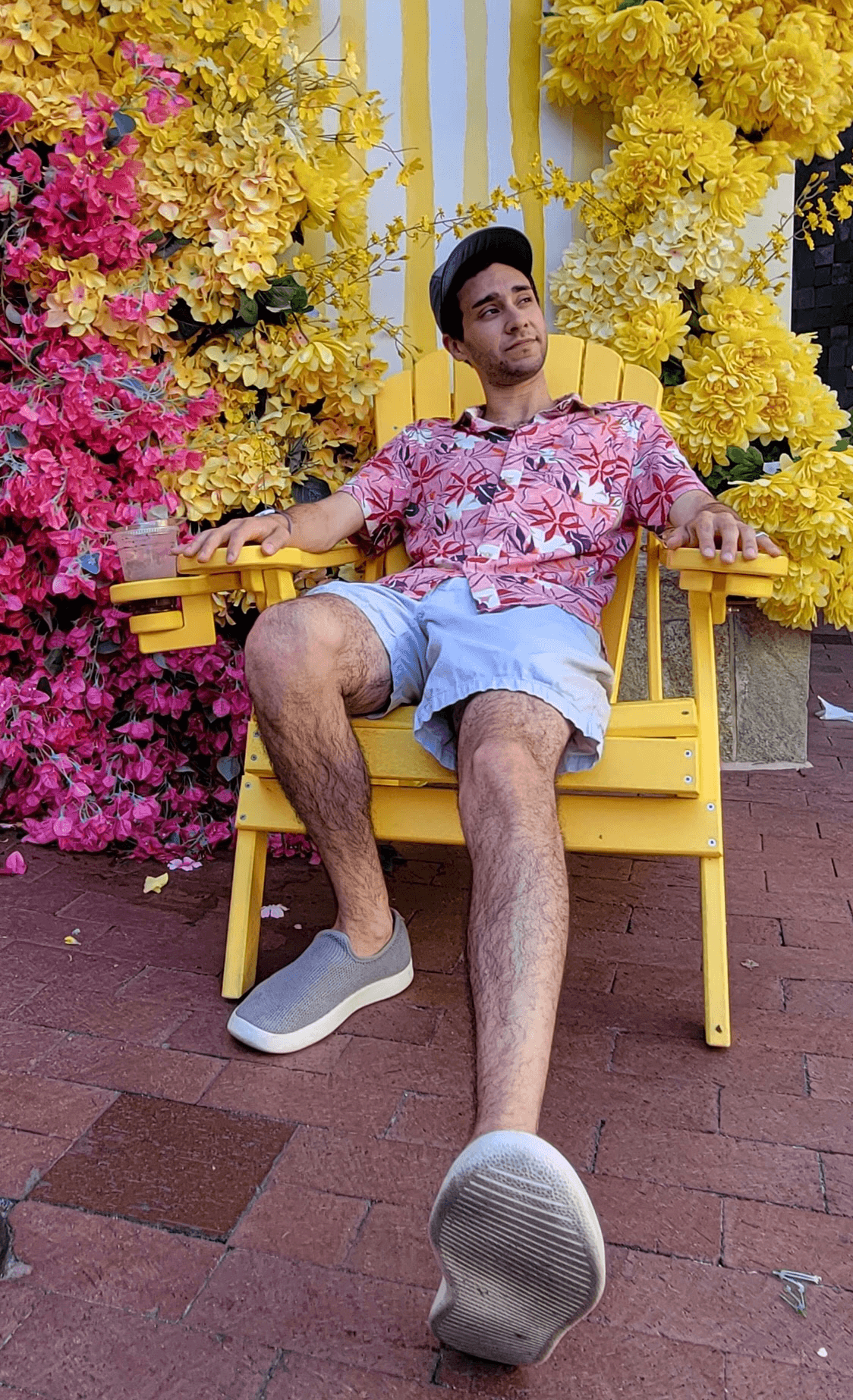 A photo of a man sitting in a wooden chair outside; in the background and multicolored flowers