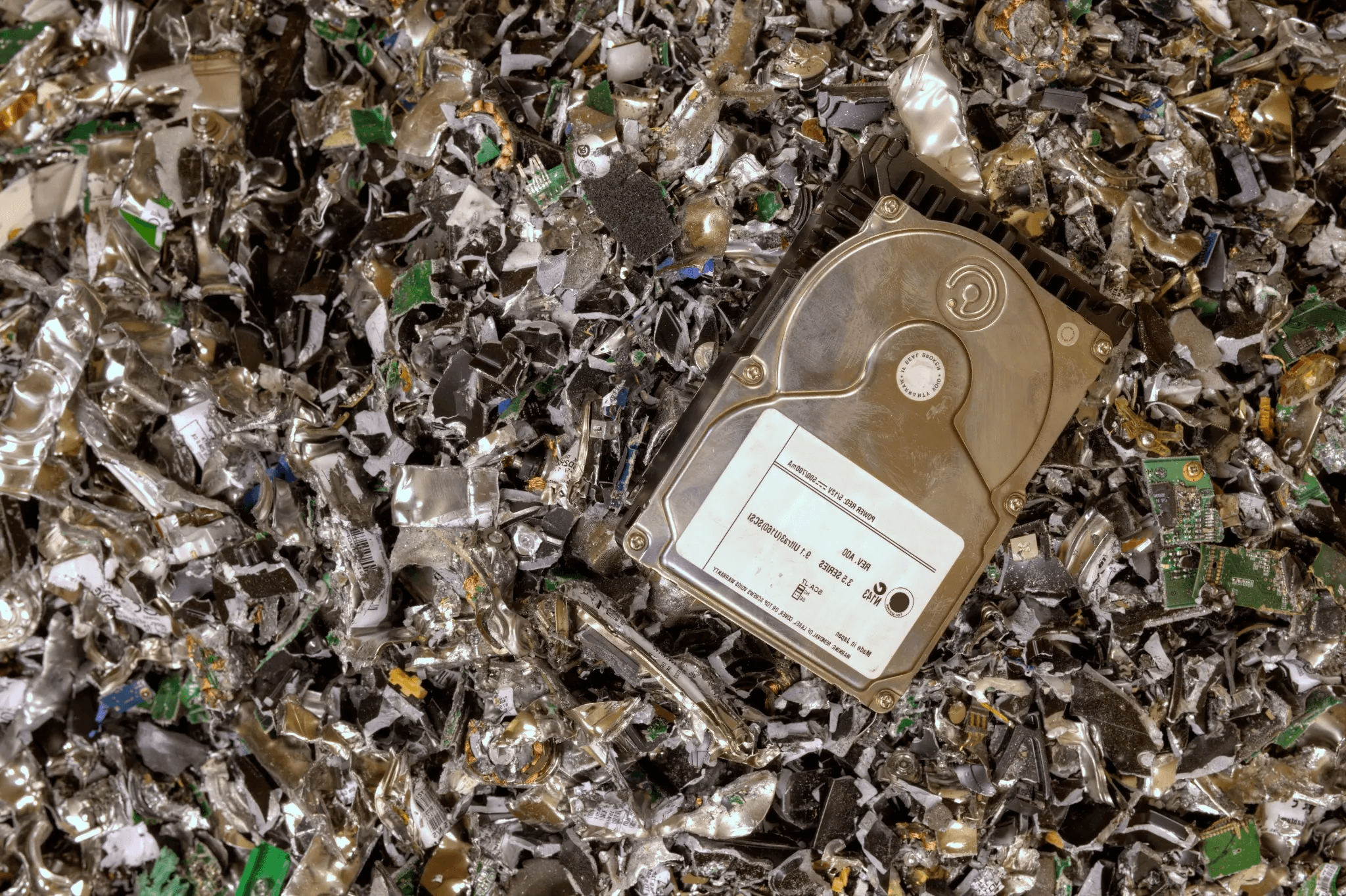 Hard drive on a pile of shredded electronic waste, representing secure data destruction and hard drive shredding services.