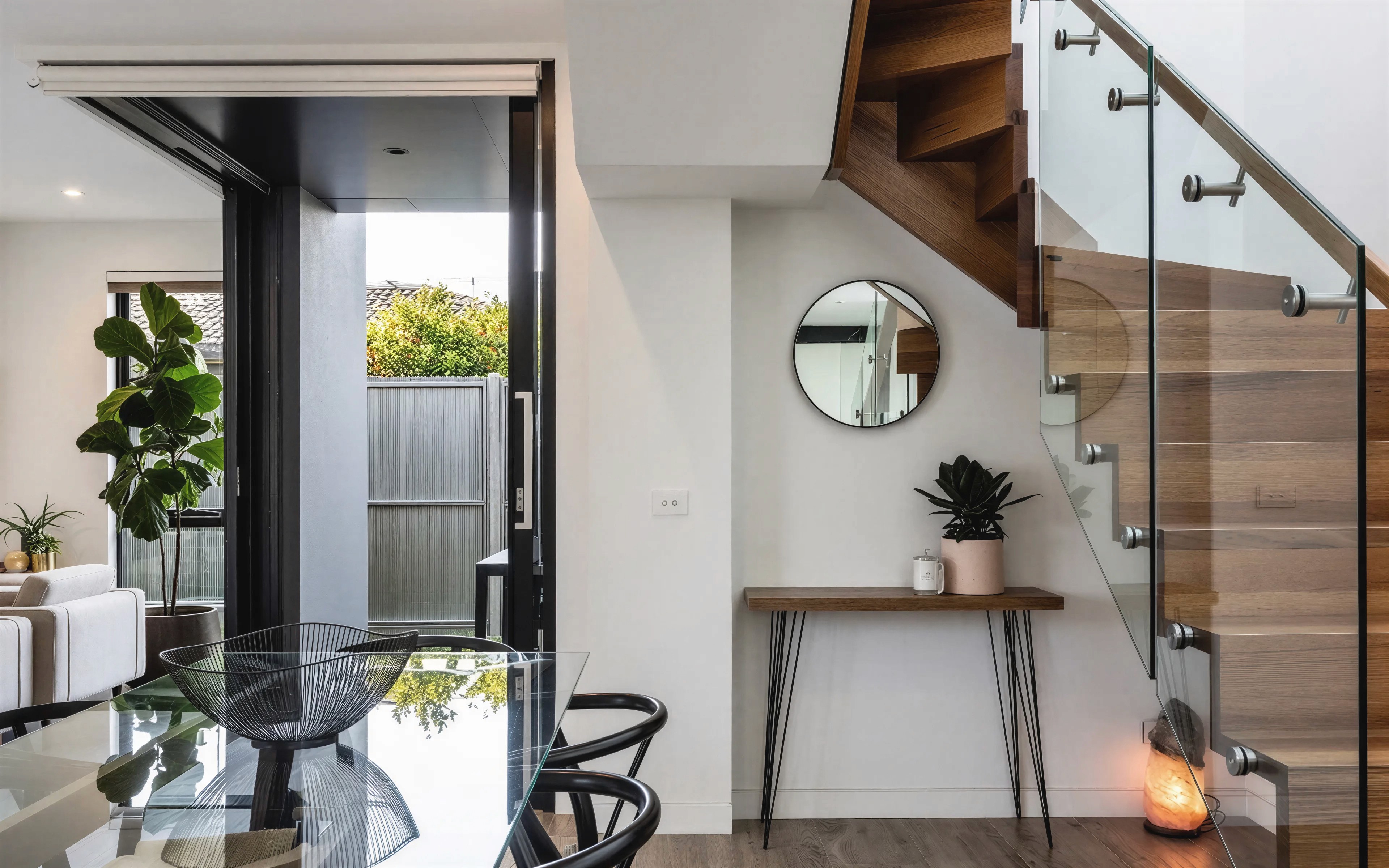 Dining area with timber staircase and glass balustrade at Bishop townhouse in Kingsville