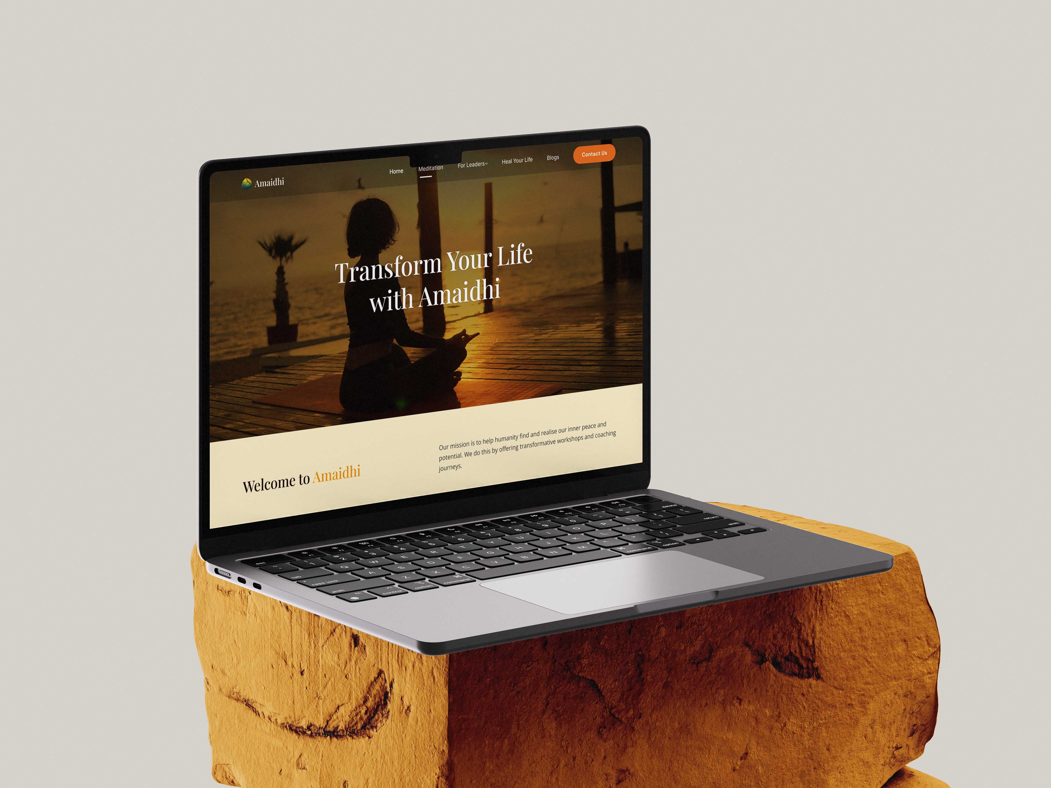 Amaidhi wellness platform website displayed on laptop showing 'Transform Your Life with Amaidhi' hero banner with sunset meditation imagery and warm golden tones on natural wooden display