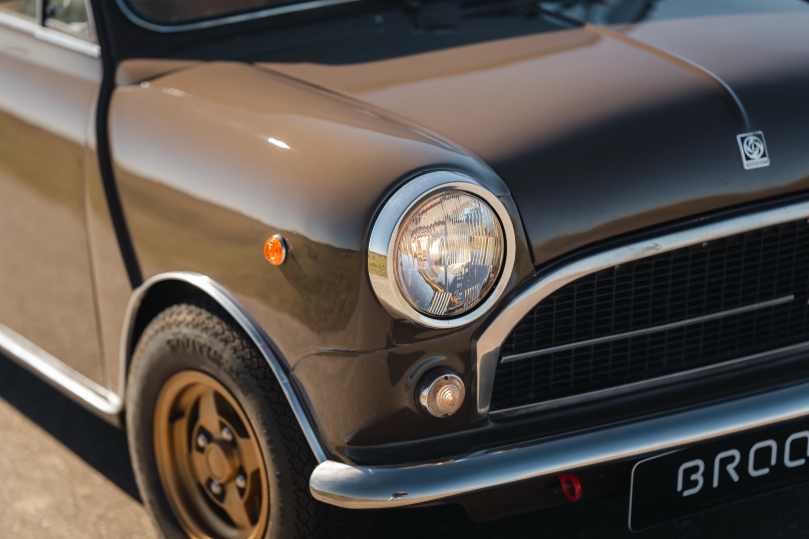 Close-up of a classic car's front, featuring a round headlight and distinctive grille design in muted colors.