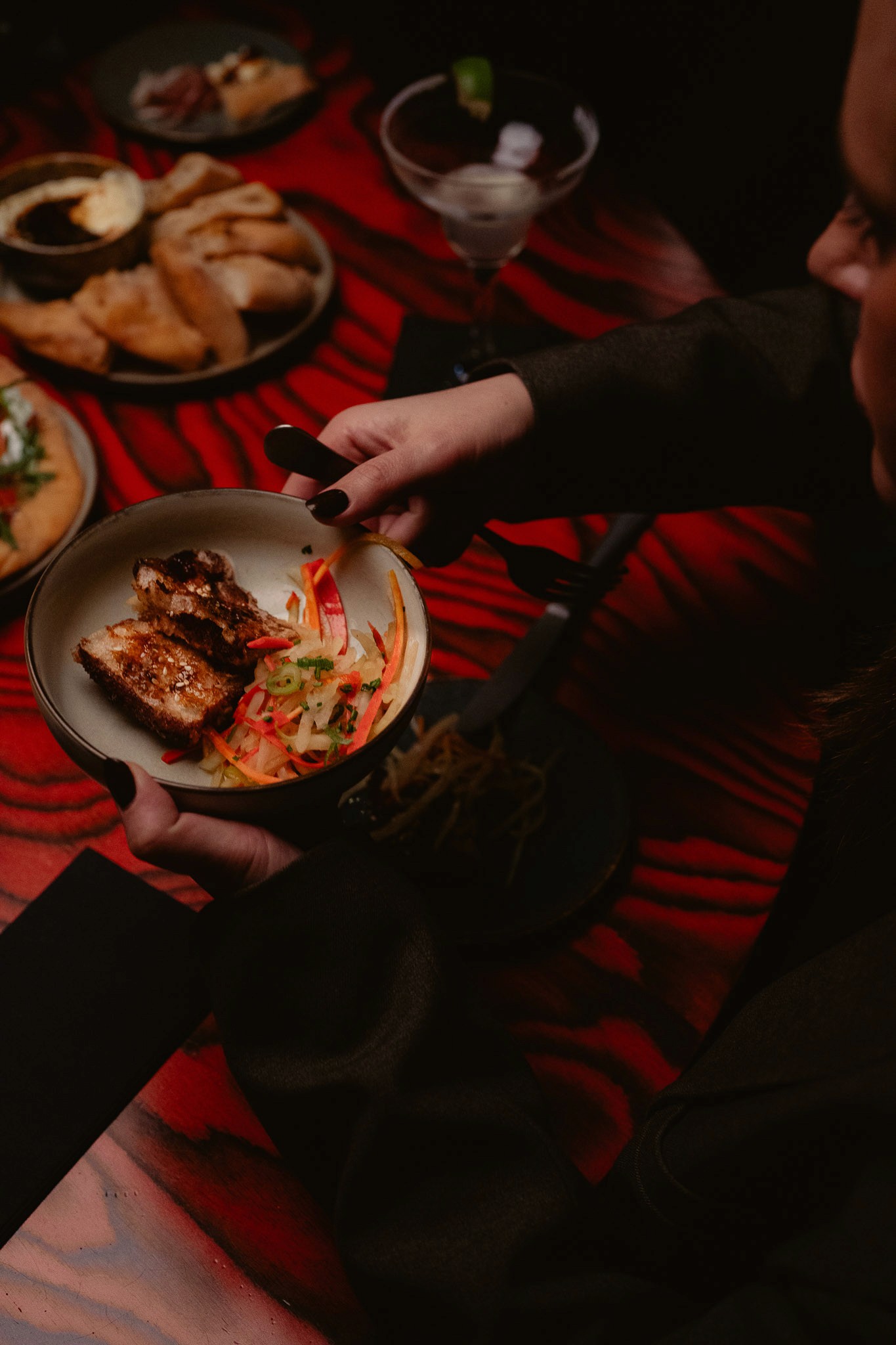 Restaurant interior with wooden tables and chairs lined against a textured wall, softly lit by round wall lamps.