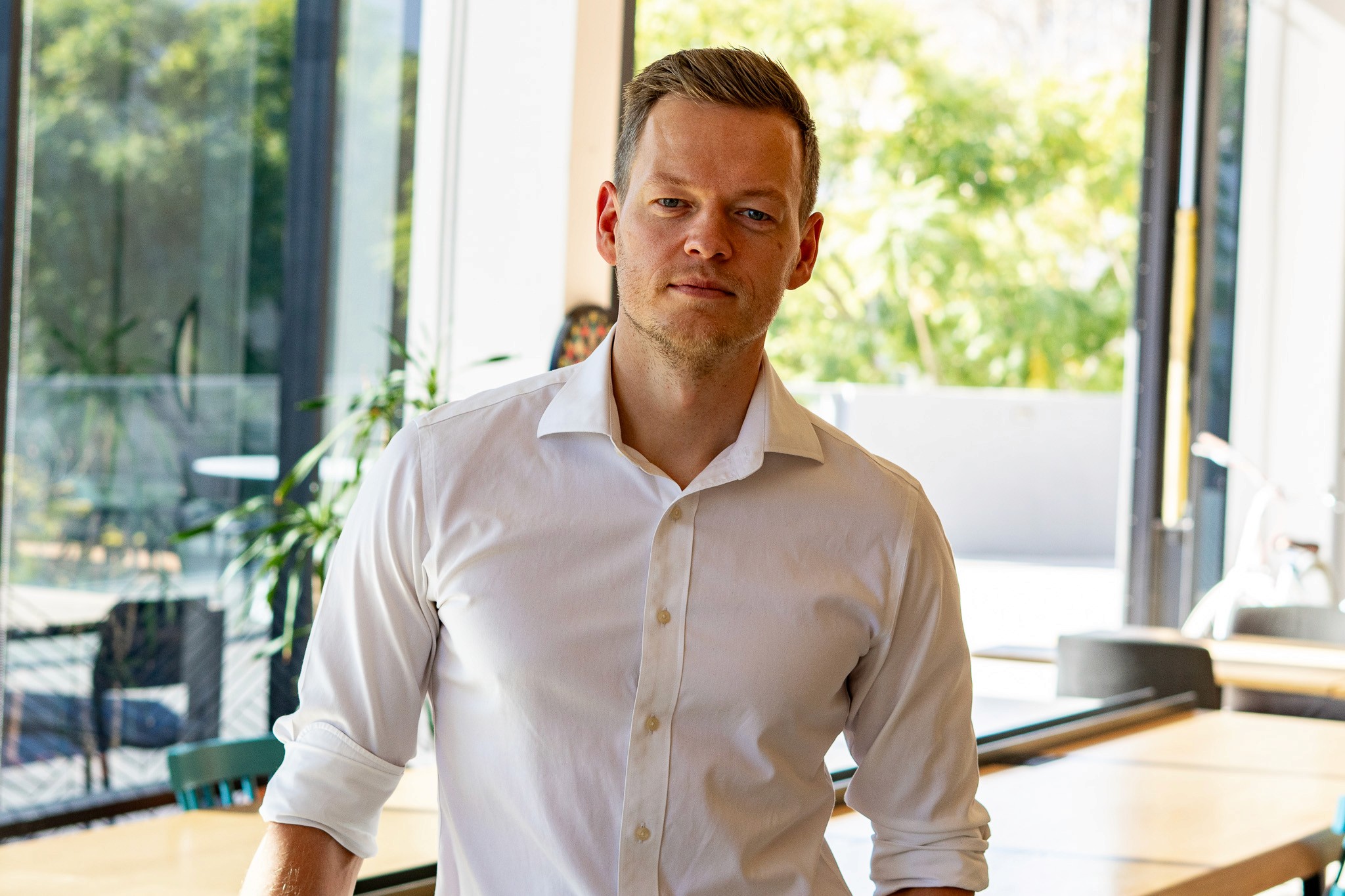 Smiling young man with short hair poses against a dark background, wearing a green button-up shirt.