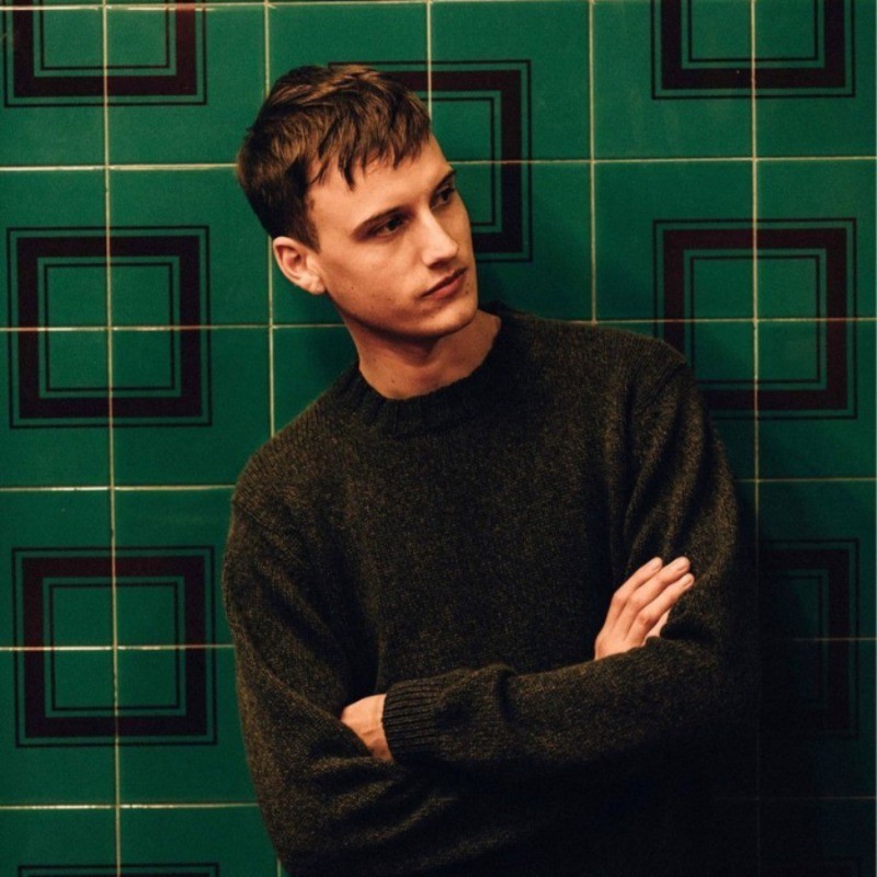potrait photo of a man looking to the side with crossed arms and a green background