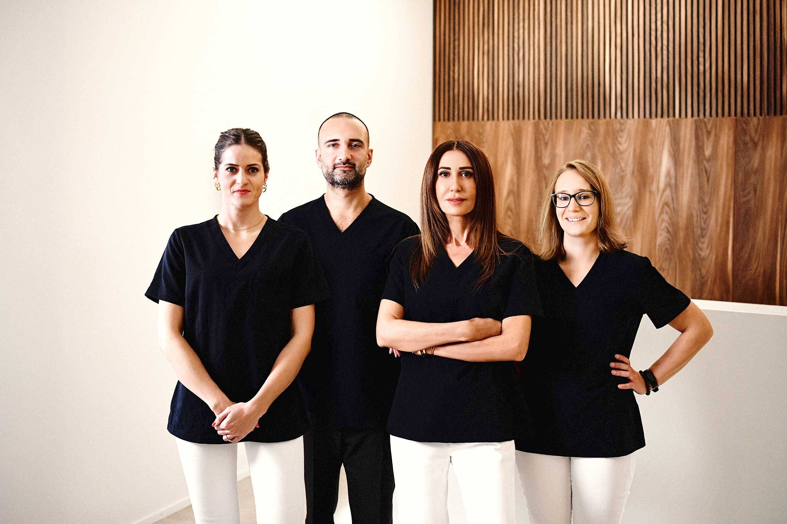 Teamfoto des Praxisteams von SpinaMed Wirbelsäulen Zentrum Muri vor einer Holzlamellenwand, vier Mitarbeitende in dunklen Shirts und hellen Hosen
