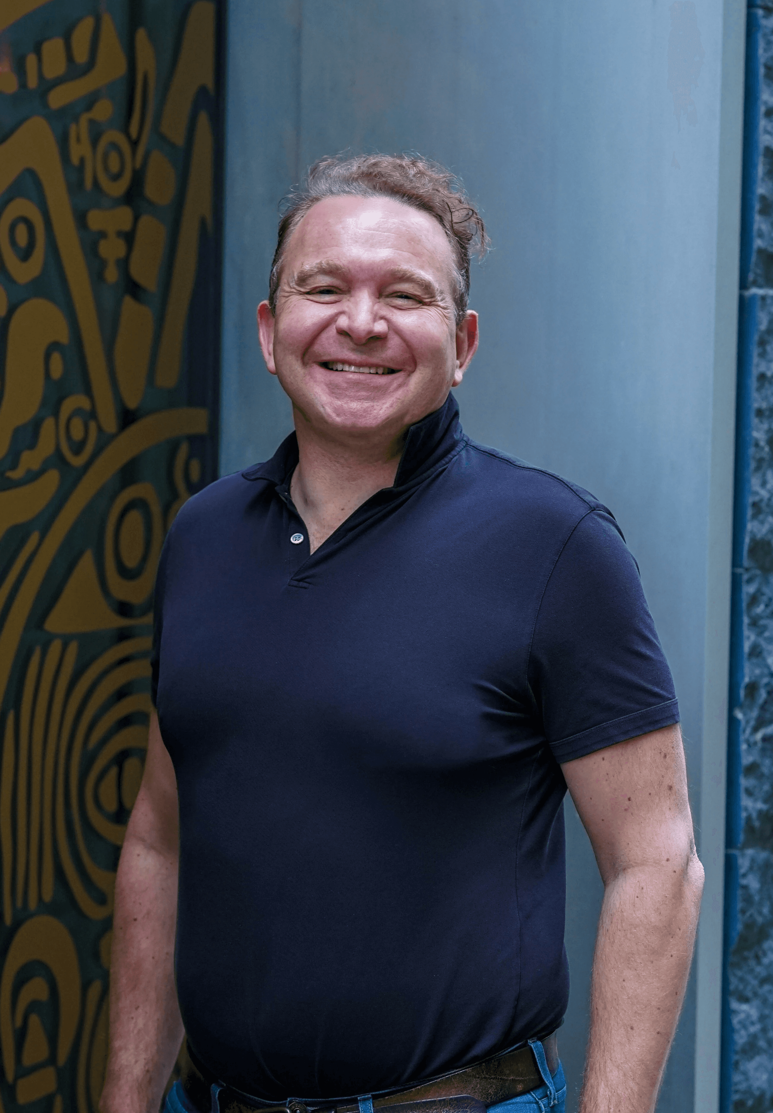 A smiling man in a dark polo shirt and jeans.