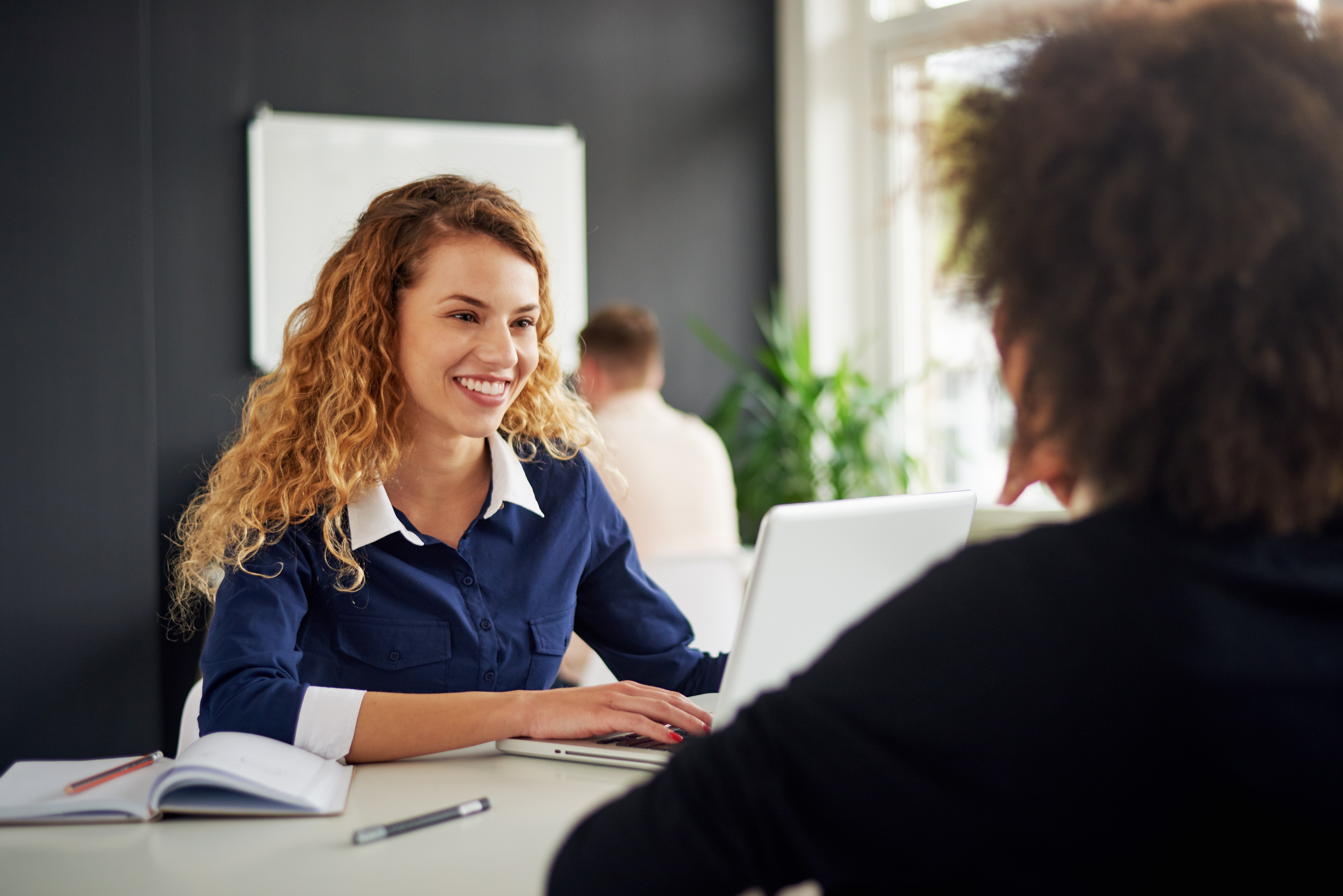 Uśmiechnięta księgowa rozmawia z klientem przy laptopie w nowoczesnym biurze.