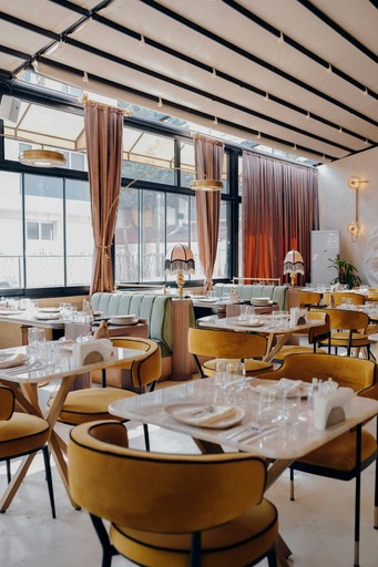 Interior moderno y elegante de restaurante con sillas de terciopelo, mesas de mármol, ventanales grandes y luz natural cálida que crea una atmósfera de comedor sofisticada.