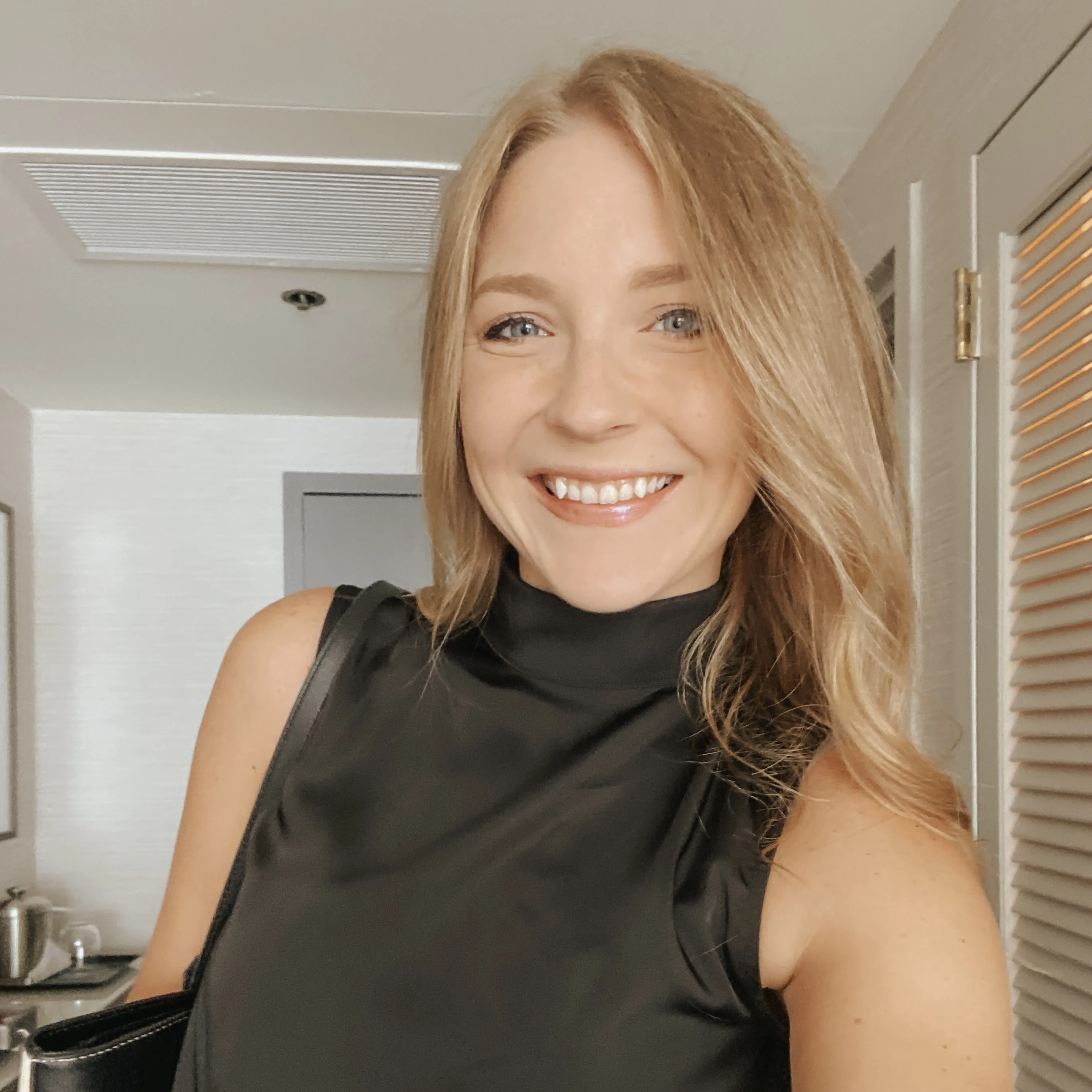 A person with shoulder-length blonde hair wearing a black newsboy cap and a black sweater.