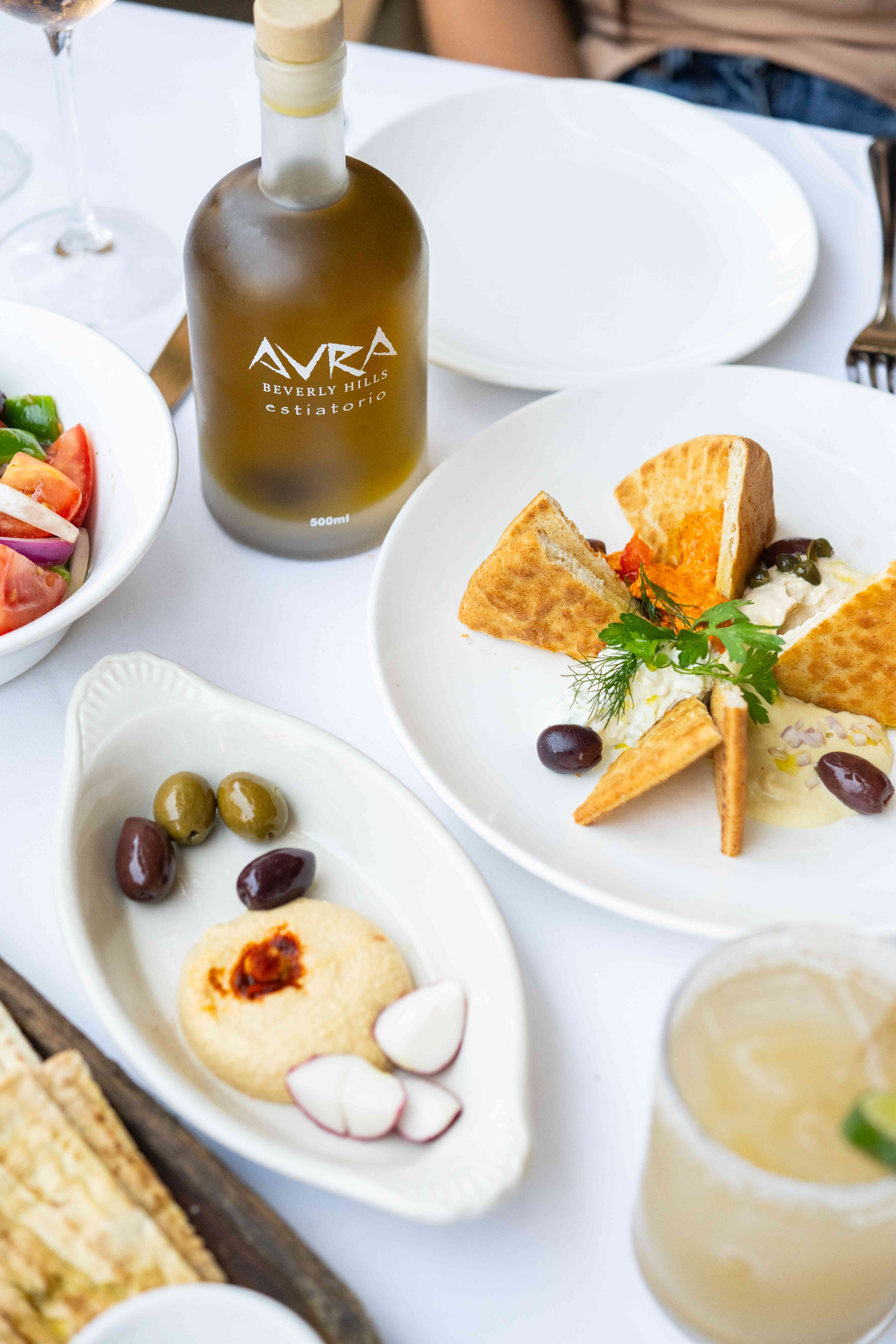 A table set with various dishes, including cheese, olives, and a bottle of oil, garnished with herbs.