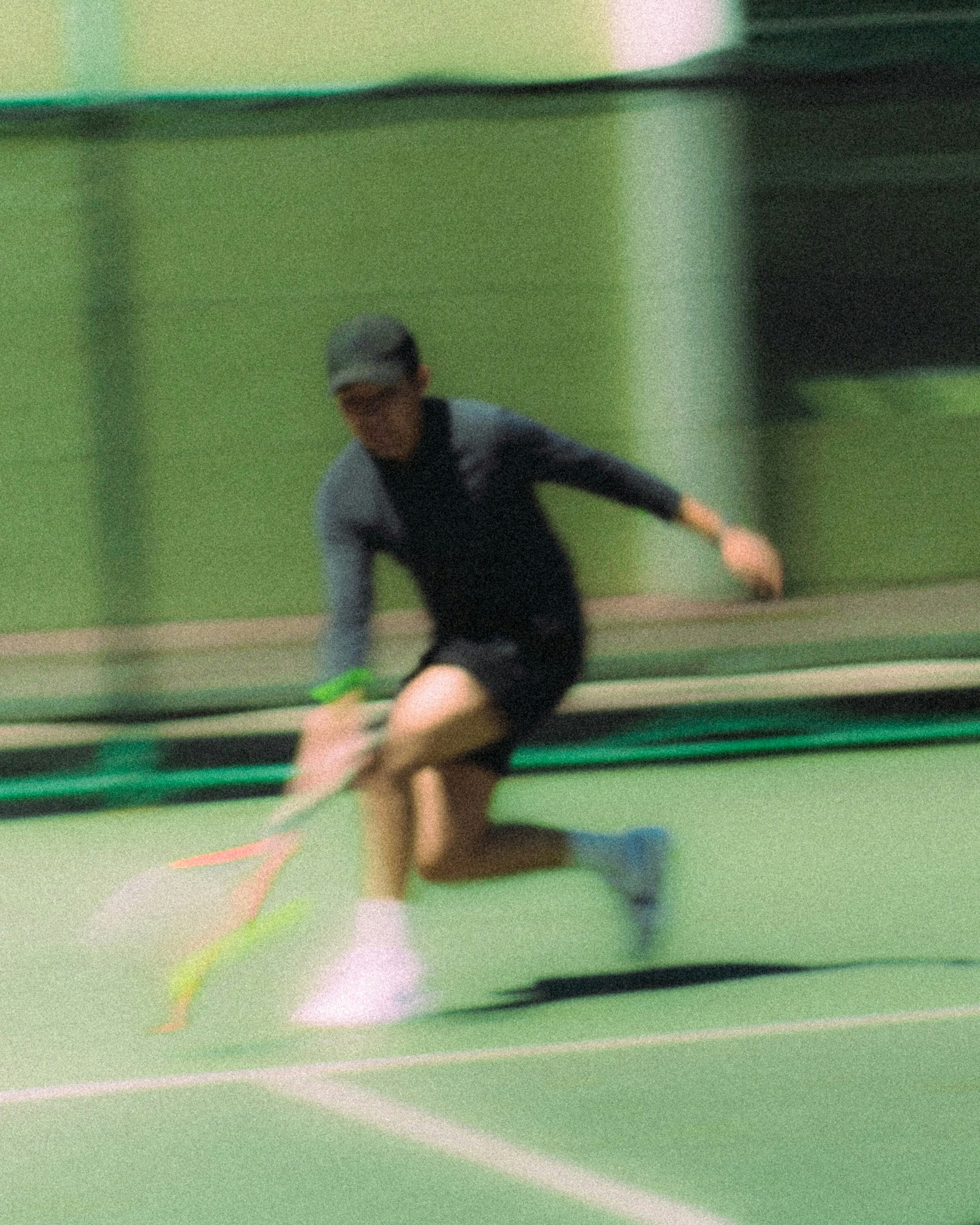 Action shot of a tennis player mid-swing on a green indoor tennis court, captured with motion blur.