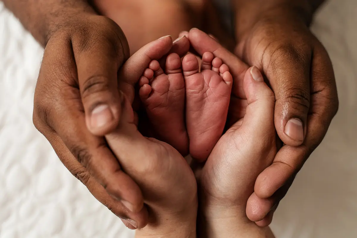 Detailní newborn foto nožiček v dlaních rodičů, památka na narození miminka.