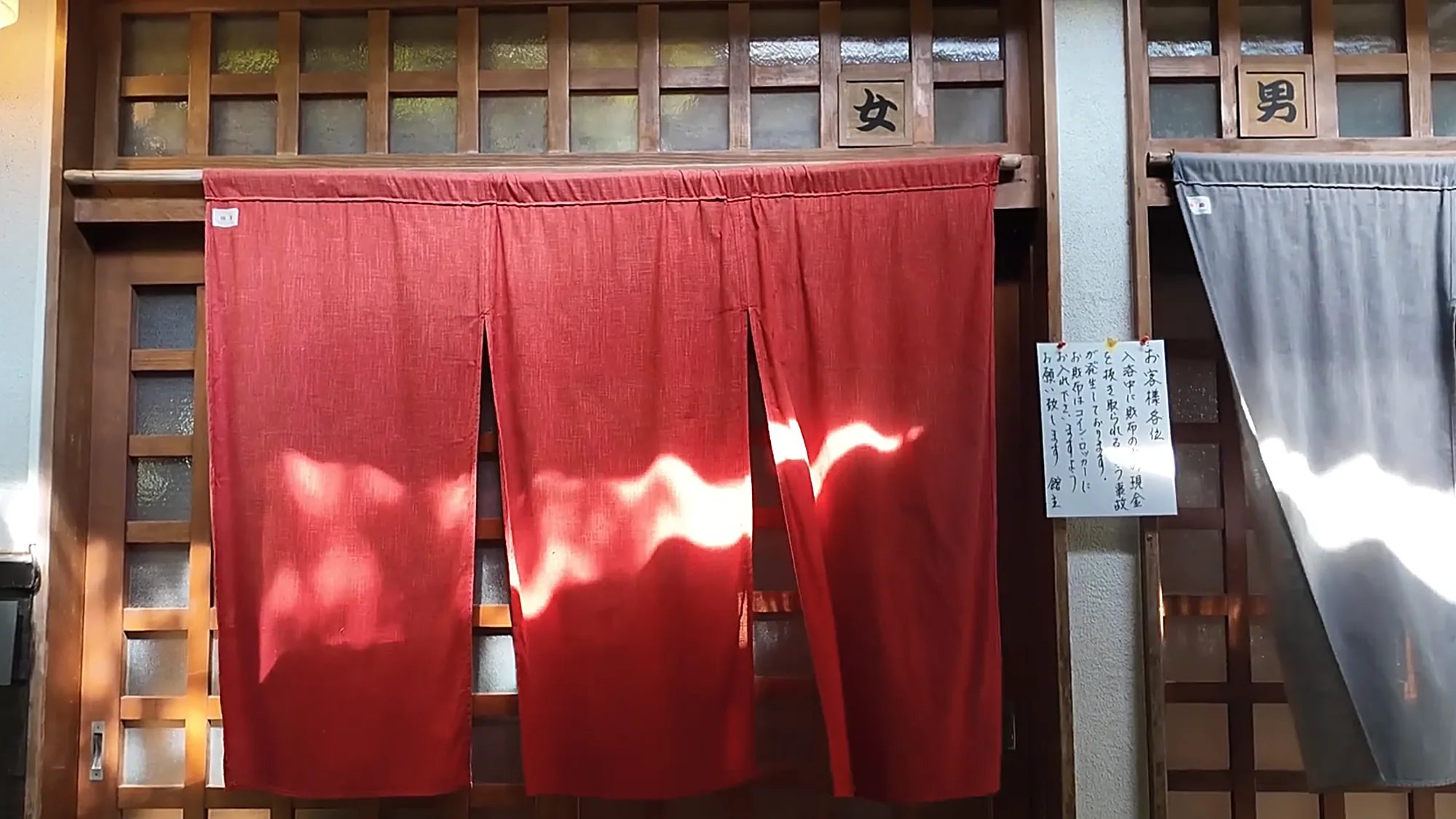 Bathhouse entrance curtains at Kurokawa Onsen: a red noren marked 女 for women beside a blue-grey one marked 男 for men