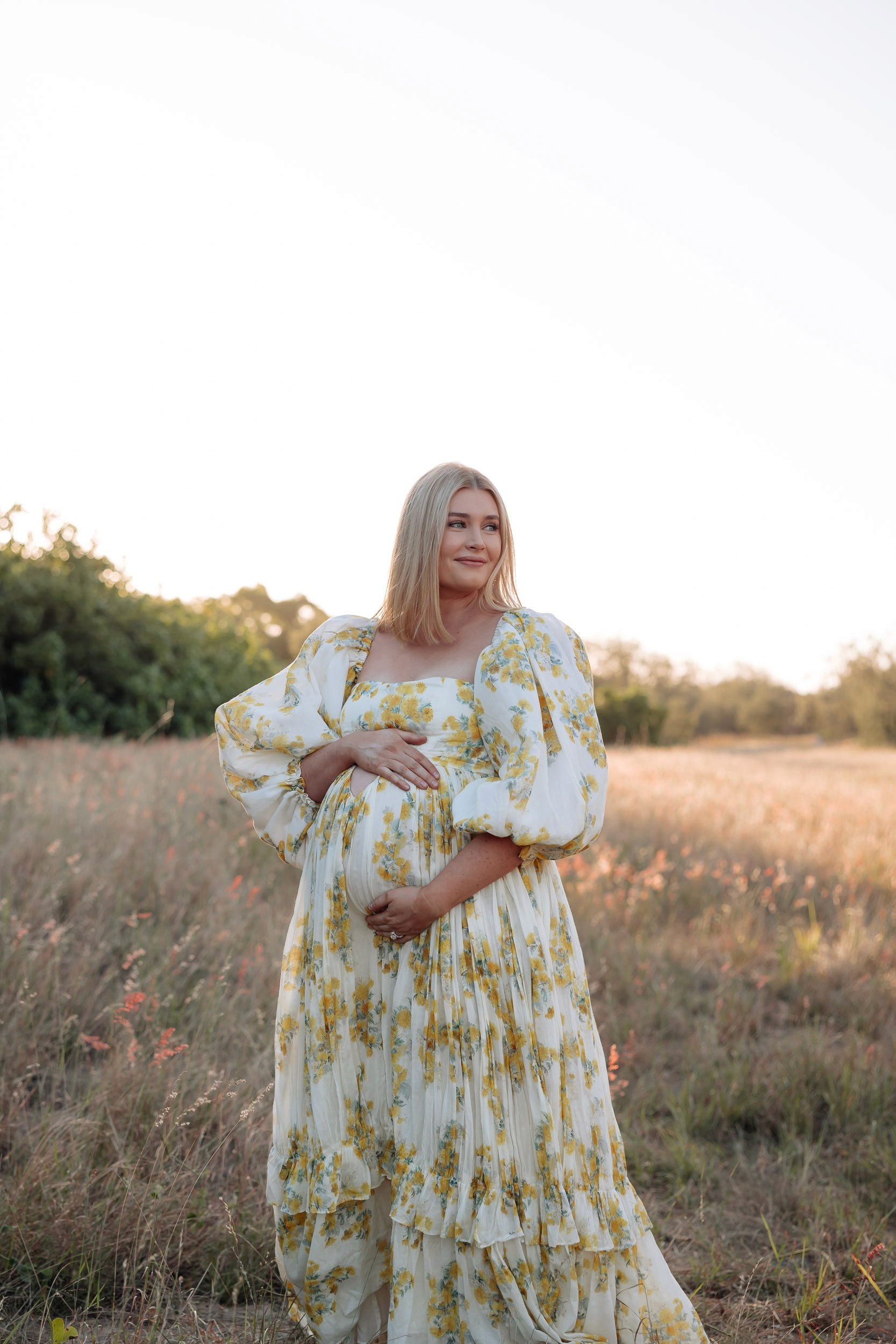 Pregnant mother holding baby bump in grassy outdoor during maternity photoshoot mackay