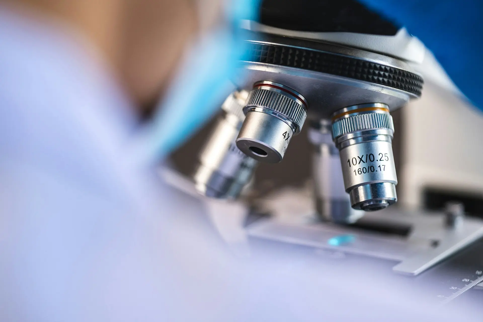 Female scientist wearing a white coat and gloves examines a sample slide in a modern laboratory setting.