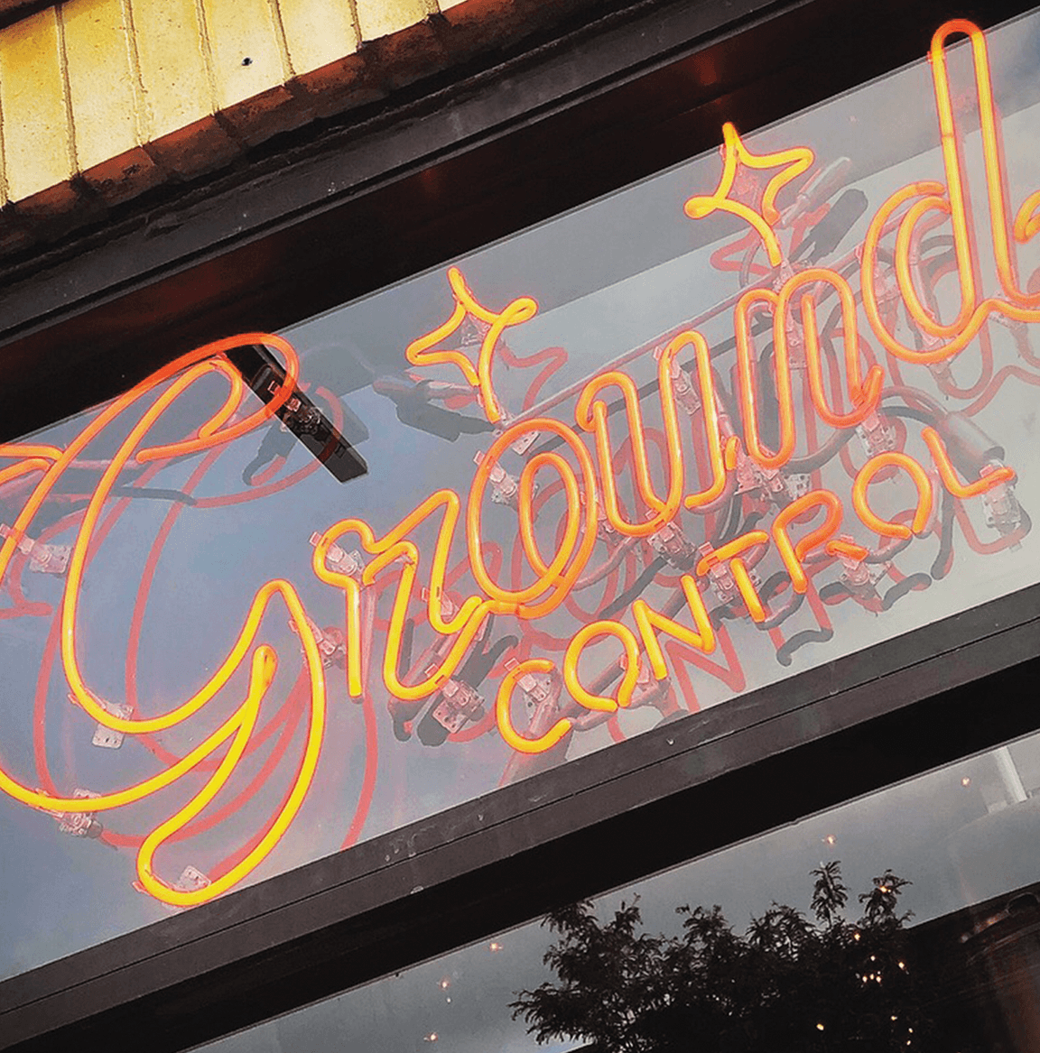 An orange neon sign of the text “Ground Control” hanging in a window