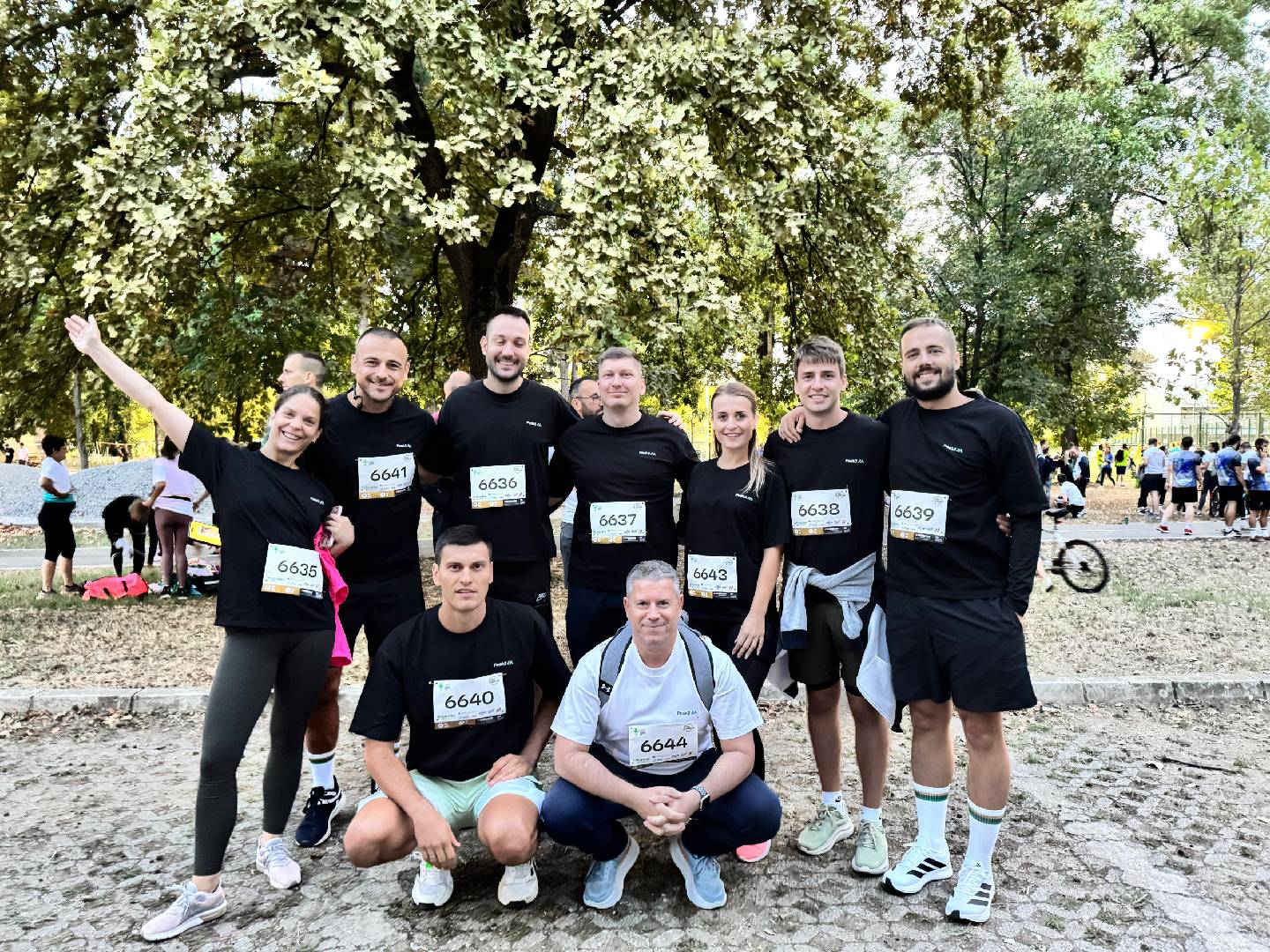 A group of eight runners poses together outdoors, all wearing matching black shirts with numbers on them.