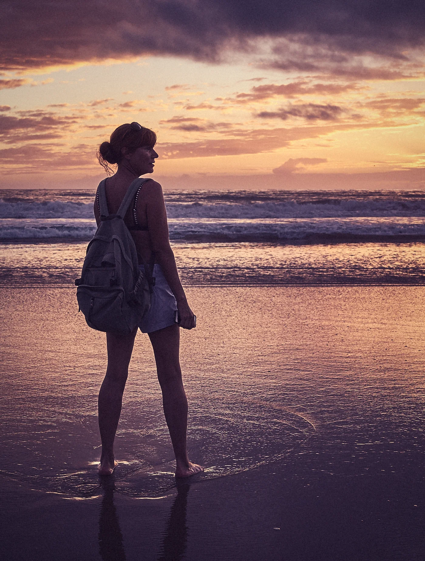 A woman stands in the sea at golden hour