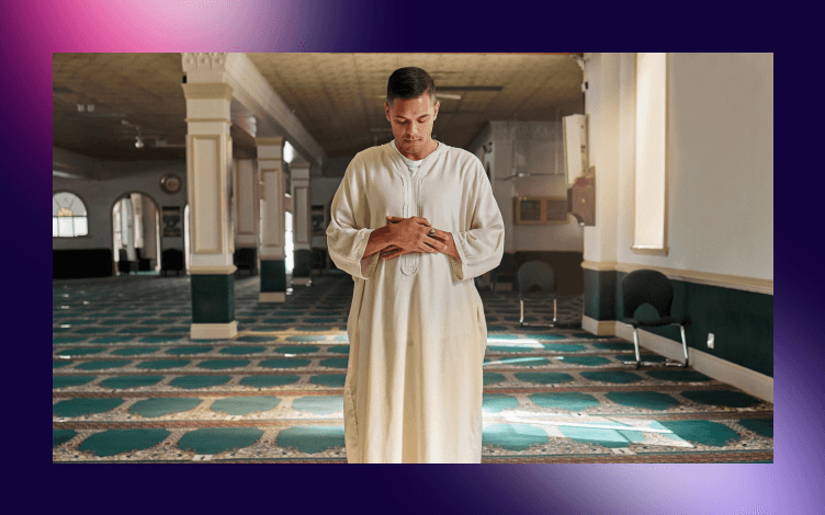 Man in traditional attire standing introspectively in prayer inside a mosque, embodying the virtue of steadfastness in religious practice.