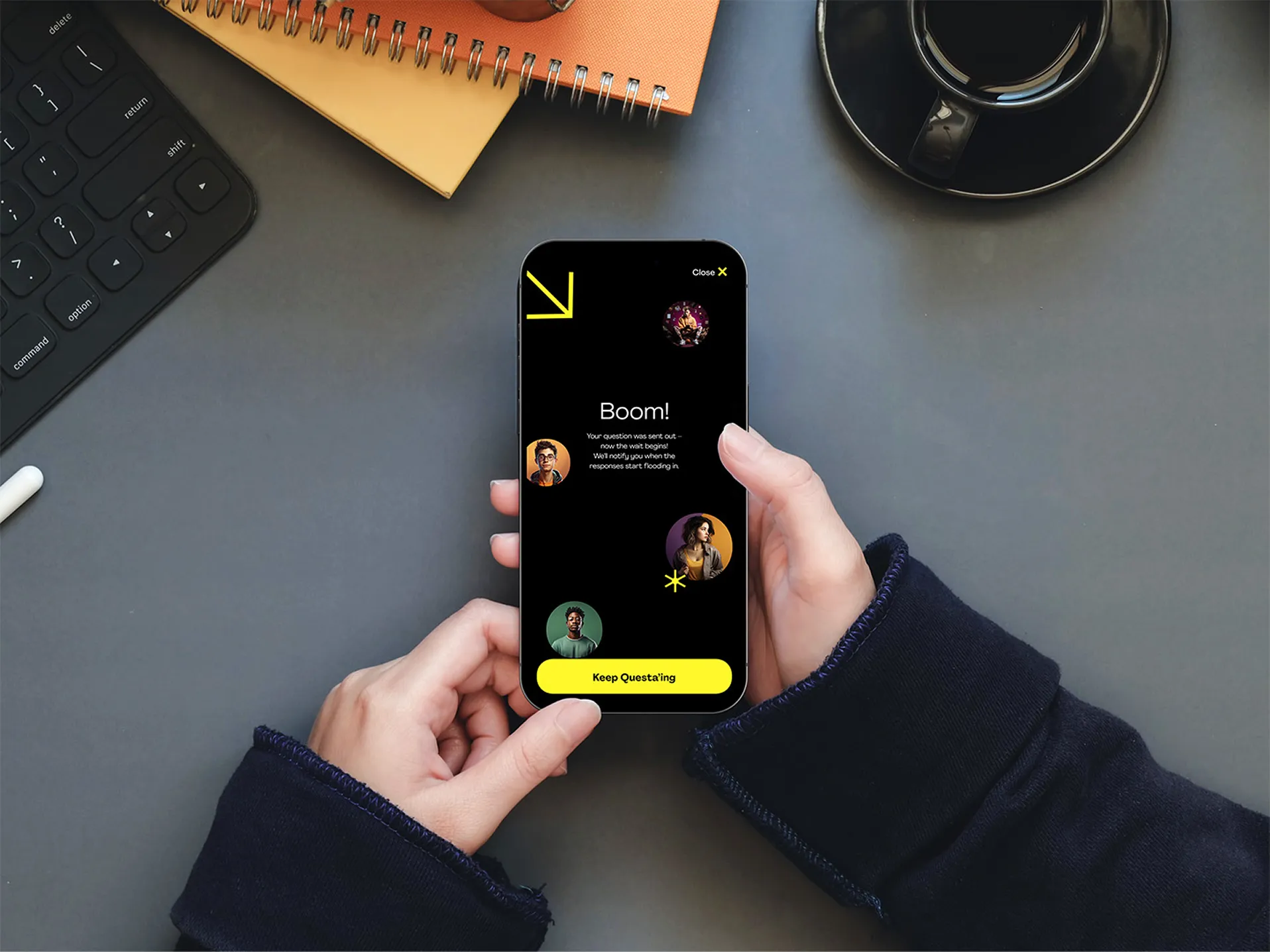 A person holds a smartphone displaying a dark screen with colorful graphics, on a desk with stationery items.