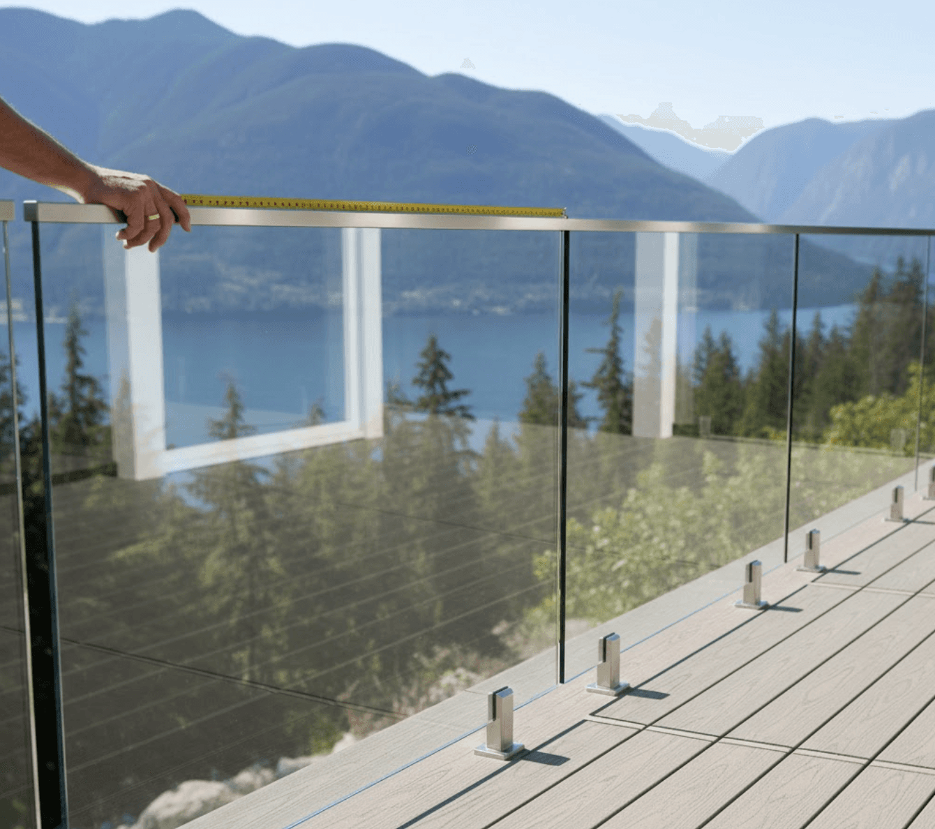 A high-quality, modern, and safety-focused photograph of a clear, frameless glass railing installed on a sleek wooden or composite deck.