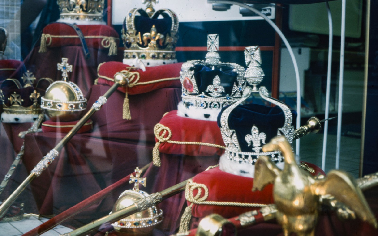 Crown Jewels display in London with crowns and scepters on red cushions.