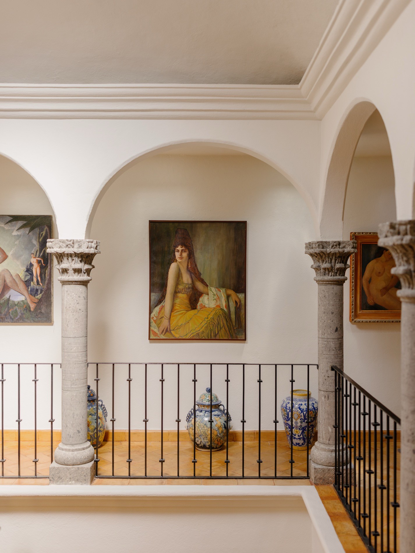 La Residencia San Miguel upper balcony gallery with oil paintings, stone columns, and Talavera vases