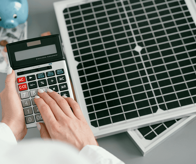 Person using a calculator next to a solar panel, related to solar tax credits.