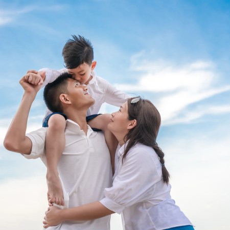 Happy family outdoors with father carrying child on shoulders and mother smiling up