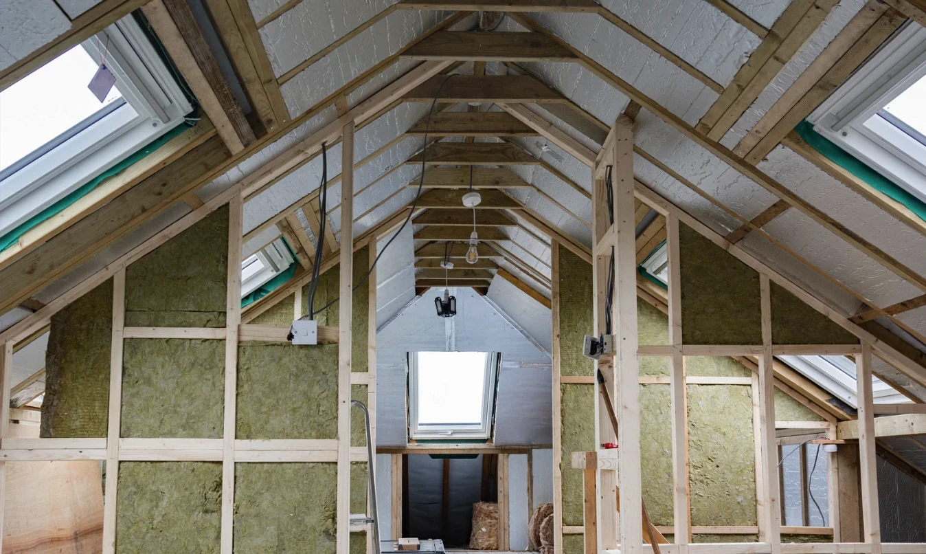 Attic under renovation with visible insulation, wooden joists and skylights