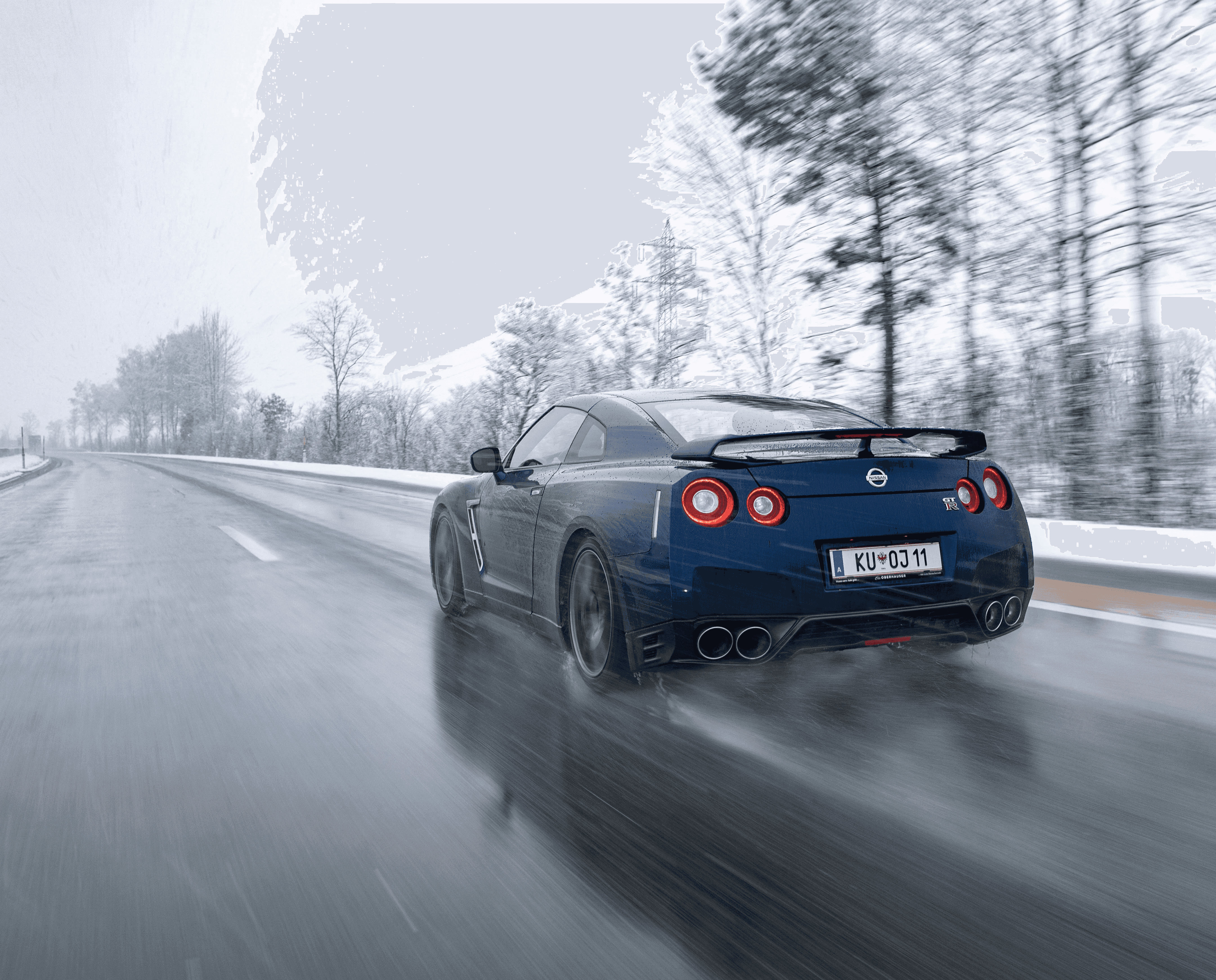 A sleek, blue sports car speeds down a wet, snowy road lined with bare trees under an overcast sky.