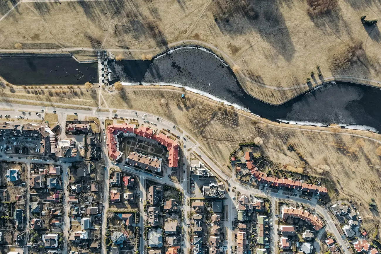High-altitude aerial drone survey view looking down on a river, roads, and residential housing layout.