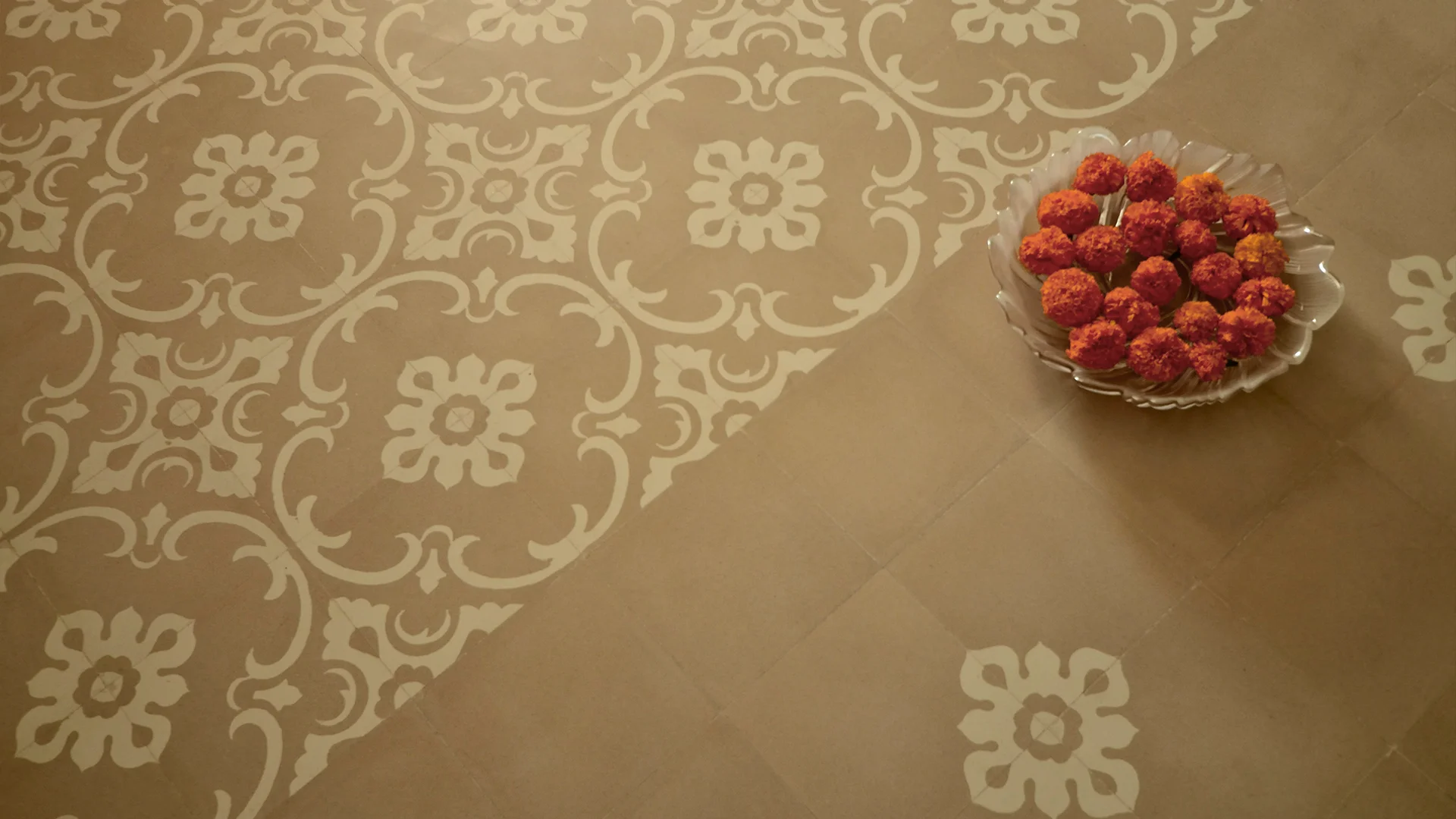 Large glass bowl filled with water and floating flowers, kept on a traditional patterned tile.