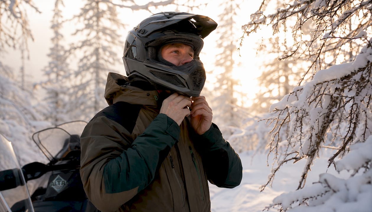 Rider fastening a snowmobile helmet strap in a snowy forest