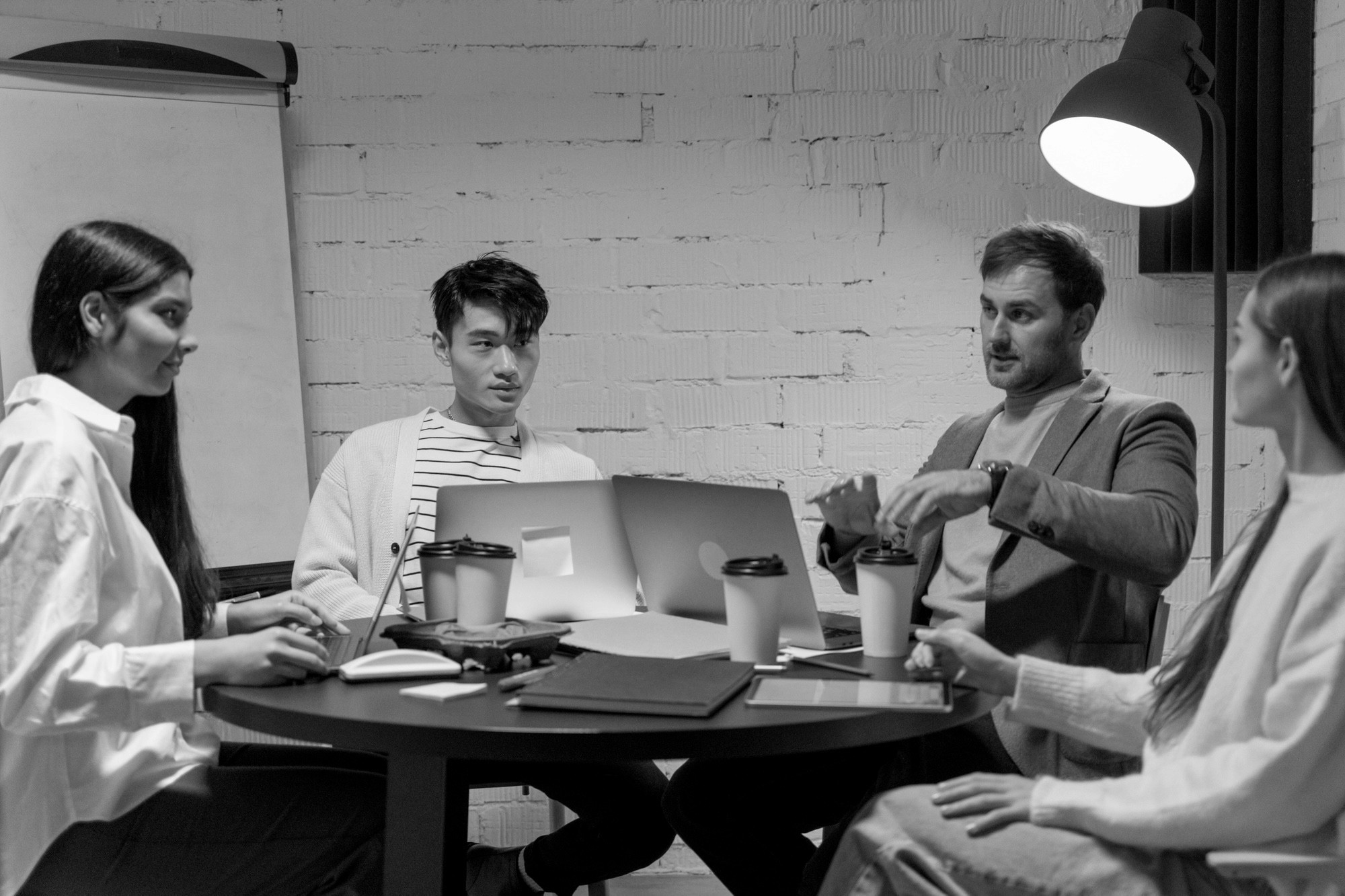 Technical team of four having a meeting around a table with a laptop and coffee in a modern office.
