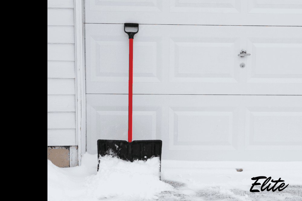 Snow piled at garage door with a shovel leaning against it, showing winter conditions that impact garage door performance.