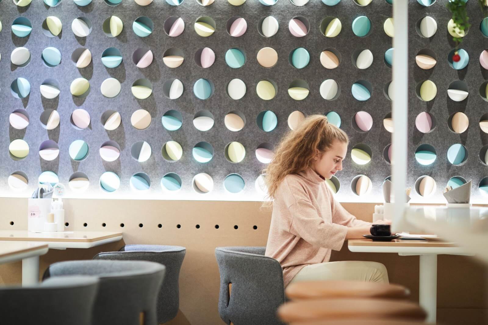 Young woman sitting in a coffee shop with bright-colored decorations in the background