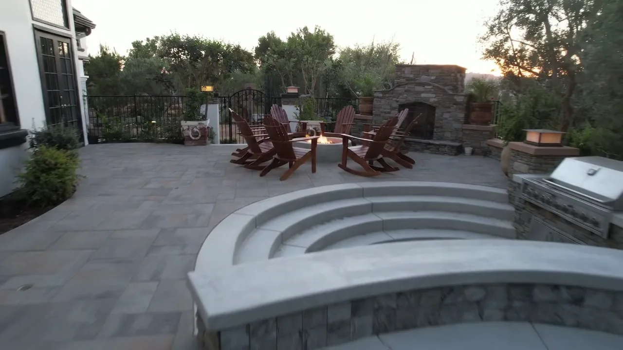 Paved patio with Adirondack seating, a fire bowl, curved steps and an outdoor fireplace beside a home.