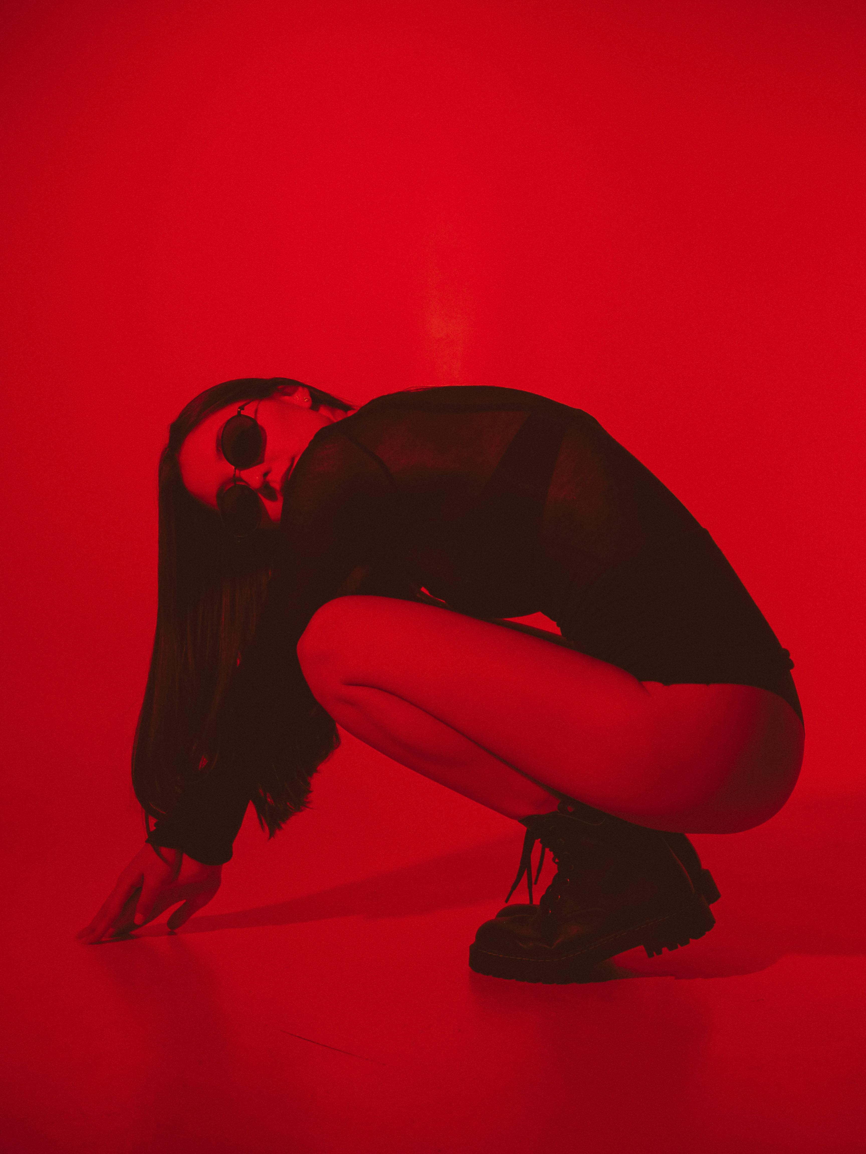 Woman wearing bent over wearing a black bodysuit and black sunglasses, red filter over image
