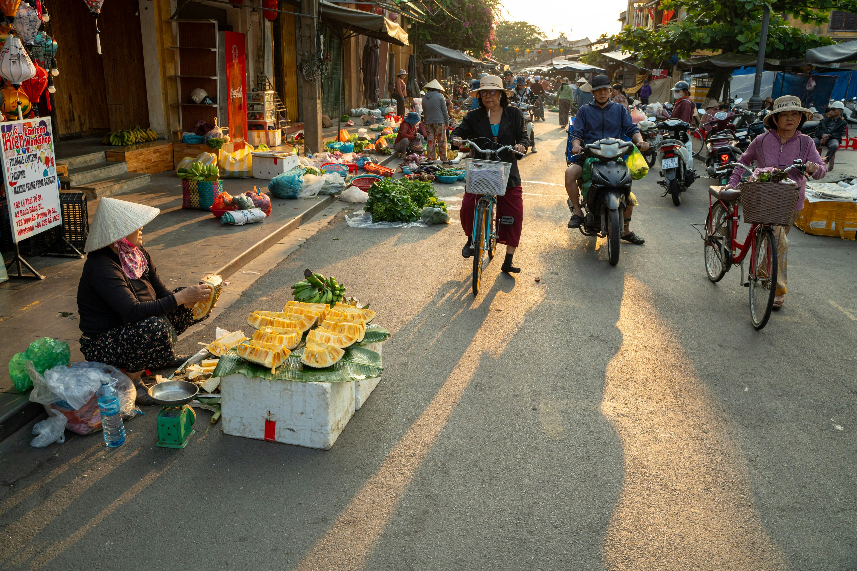 Street market scene with vendors and cyclists at sunset.