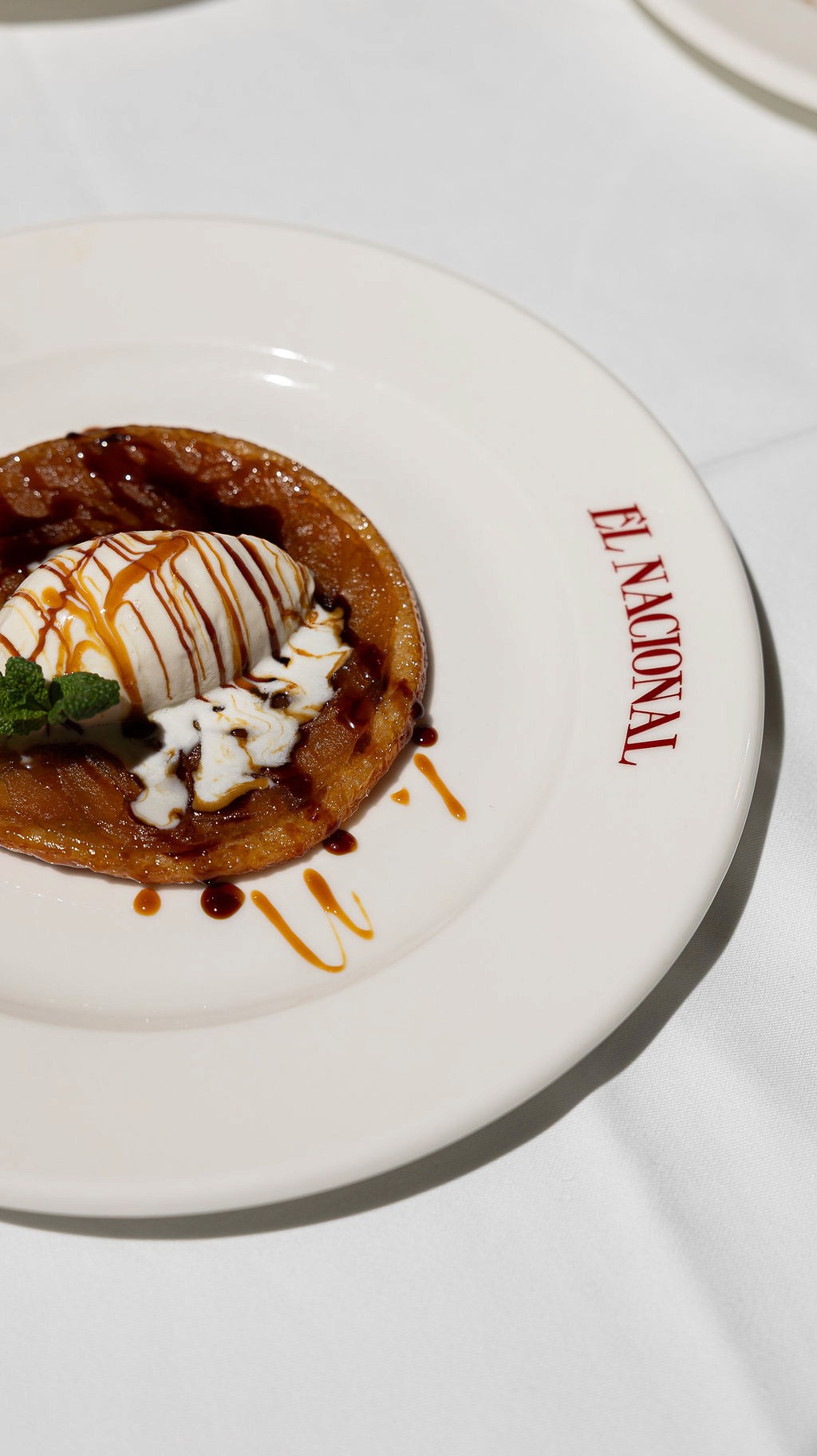 Person with a mustache wearing a black t-shirt carrying a tall stack of pizza boxes inside a dimly lit bar or restaurant.