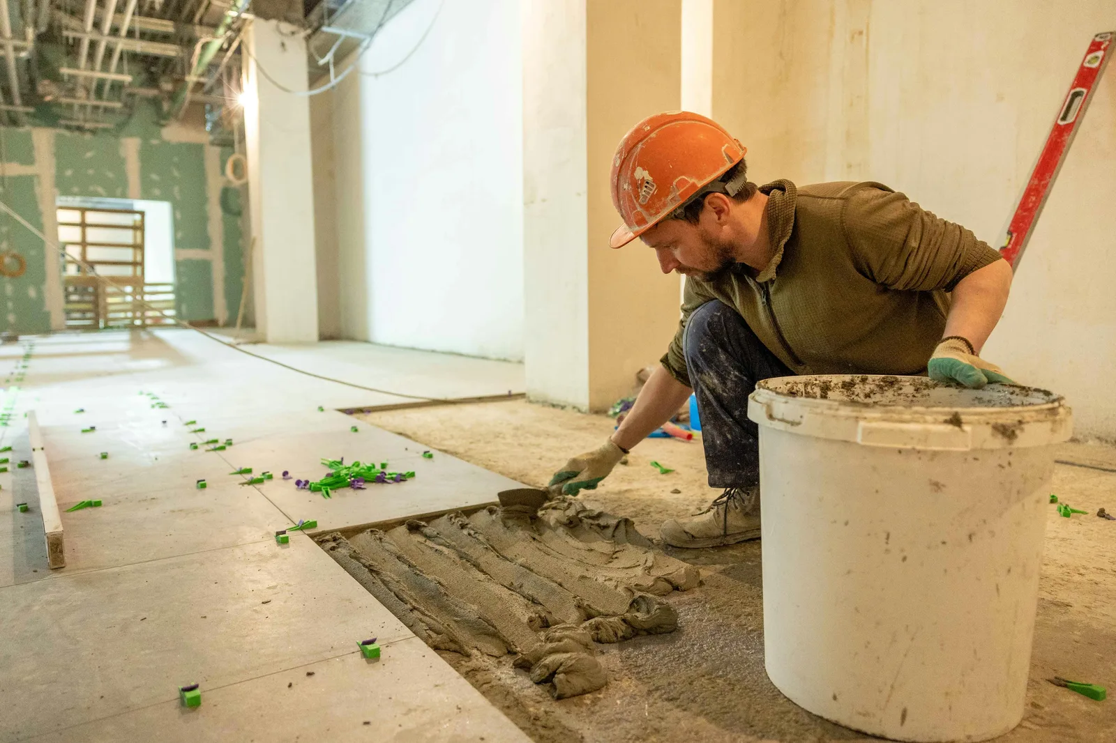 Worker in hard hat spreading adhesive mortar on large floor area