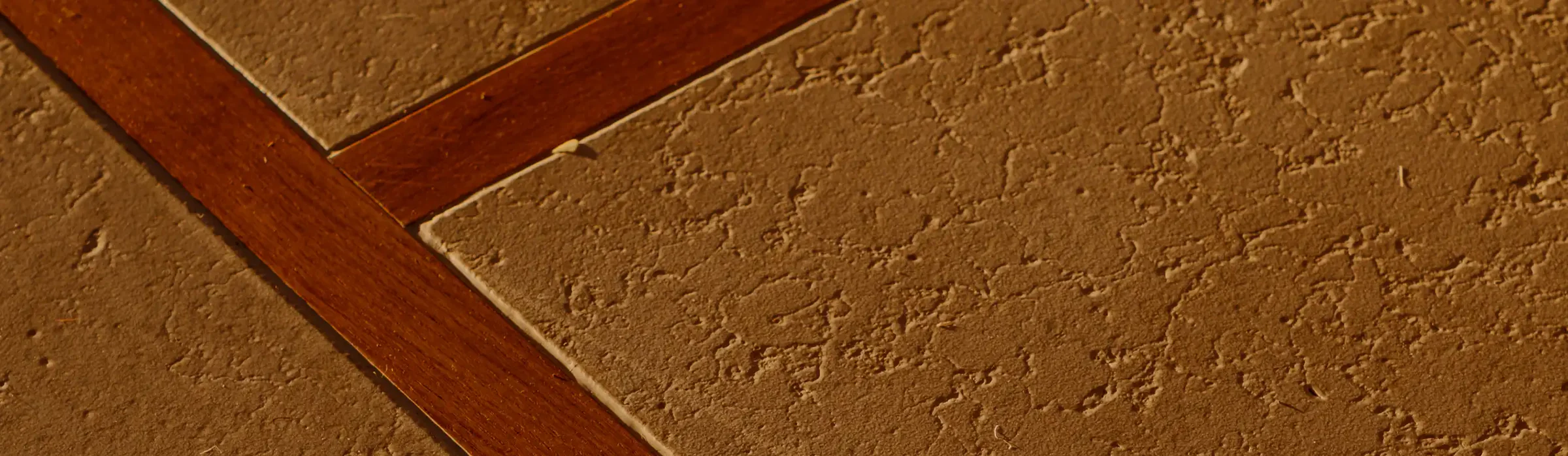 Verputzte Bodenplatten mit einer rotbraunen Holzfuge dazwischen