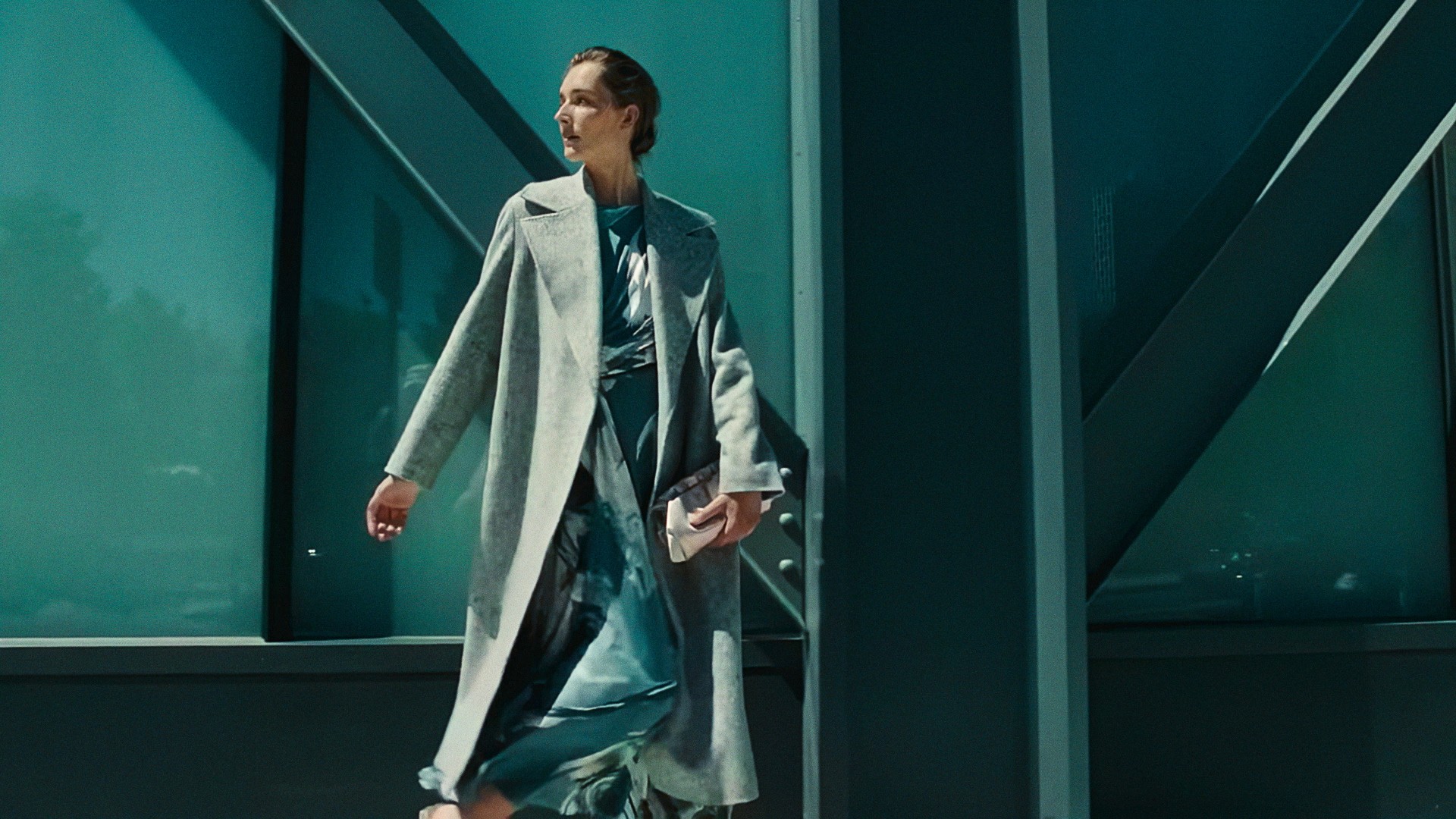 A woman in a long gray coat walking past teal steel beams, Lafayette 148 New York