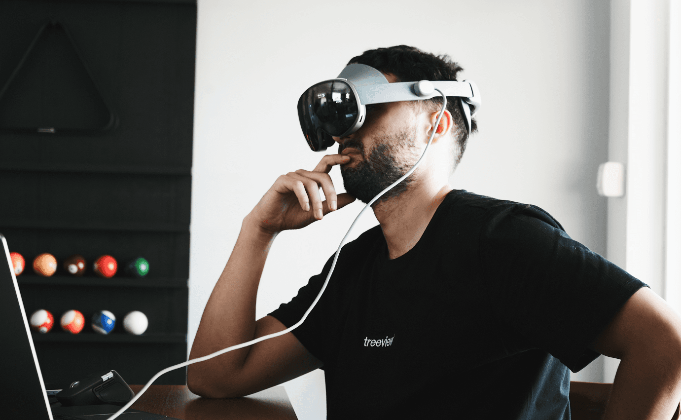 Treeview developer wearing a mixed reality headset at a desk, hand raised to chin in a thoughtful pose, with billiard balls visible in the background