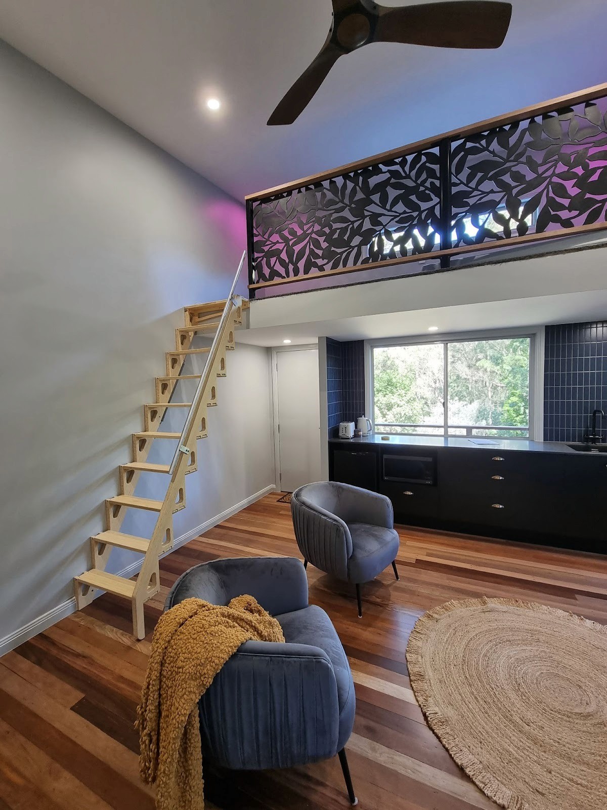 Modern loft interior with wooden staircase, mezzanine railing, cozy seating area, and minimalist kitchen design